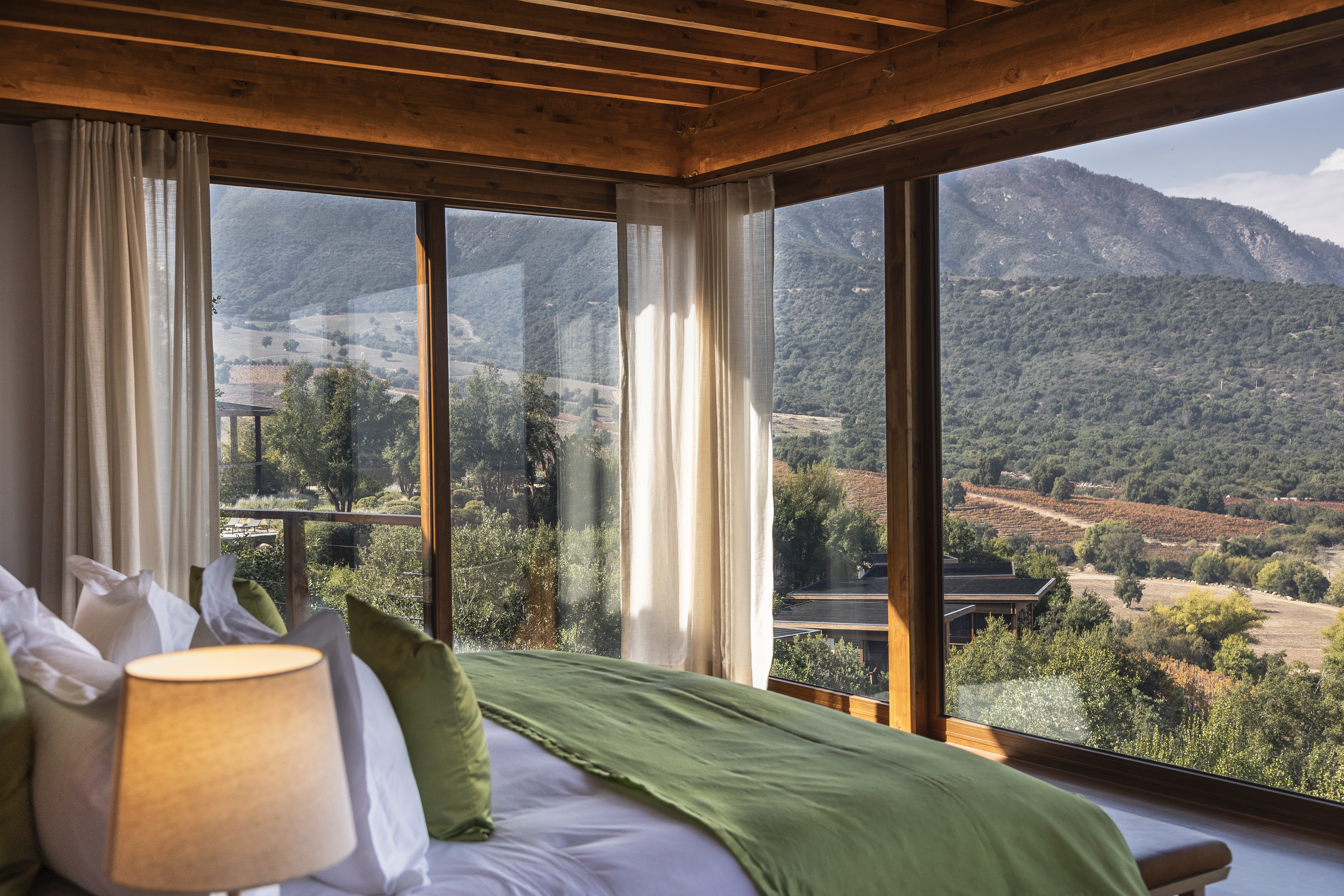 A wood-lined bedroom frames vineyard slopes and mountain views through tall windows at Clos Apalta Residence.