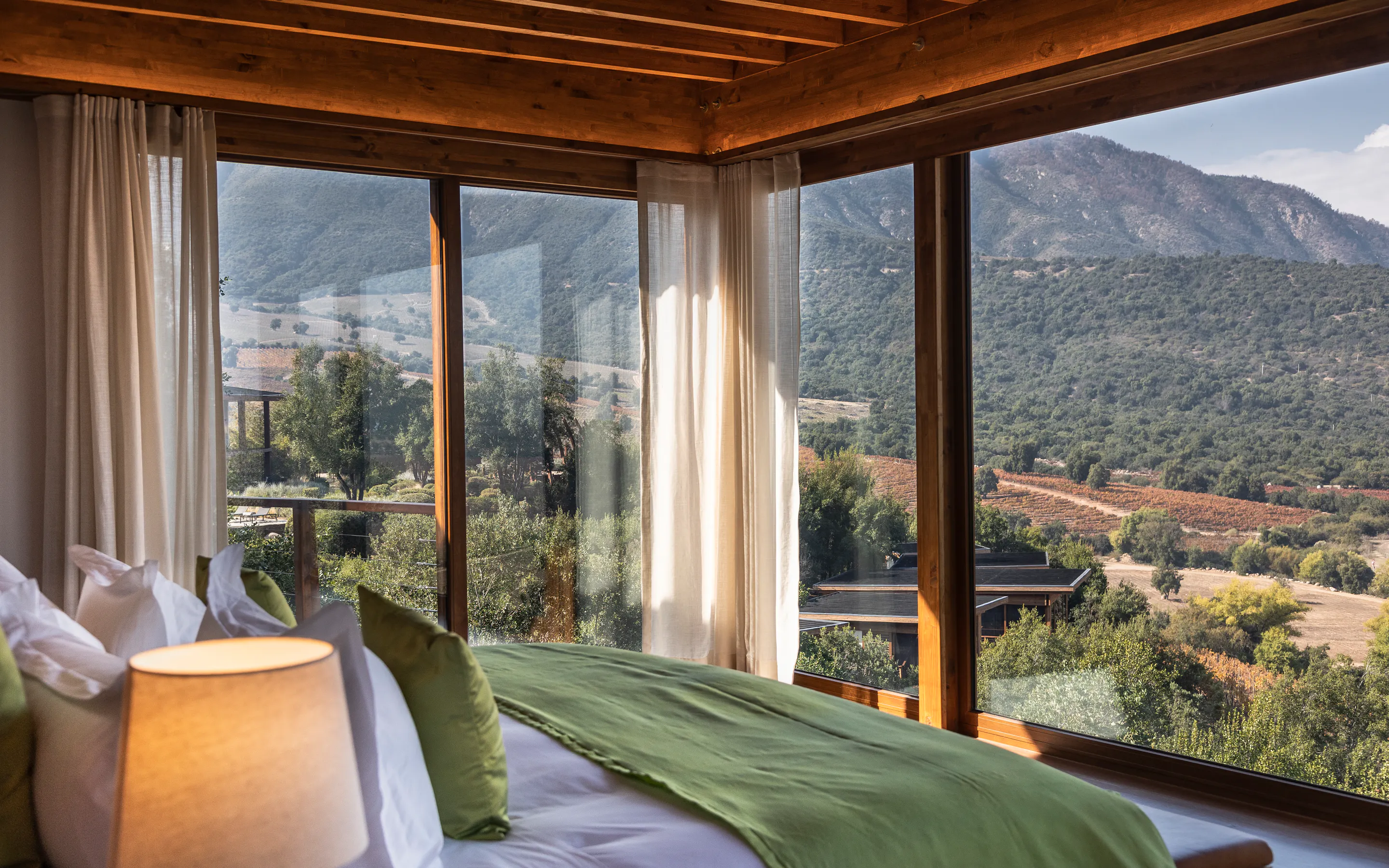 A wood-lined bedroom frames vineyard slopes and mountain views through tall windows at Clos Apalta Residence.