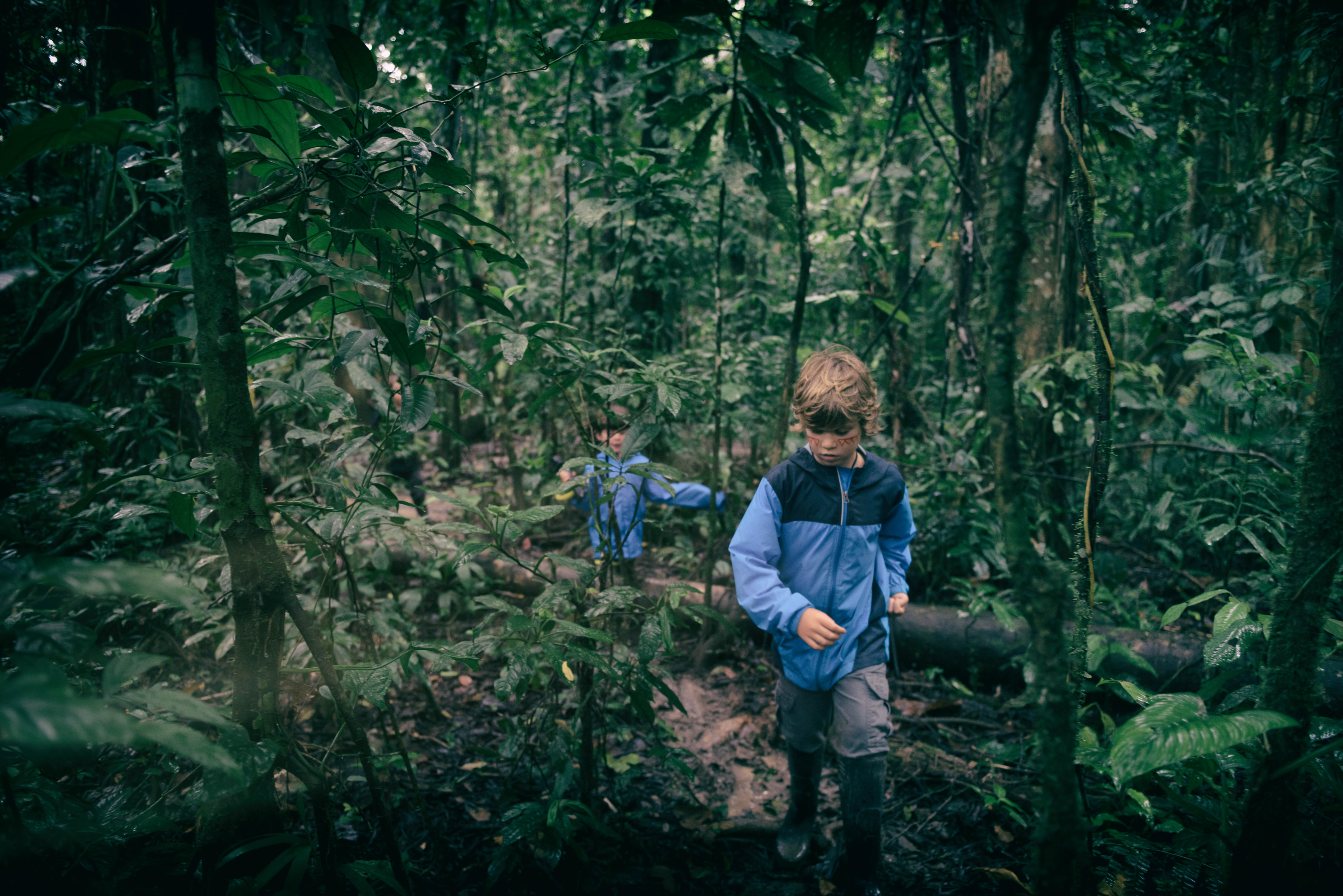 A family in rain gear walks along a forest boardwalk deep in the Peruvian Amazon, surrounded by dense greenery.