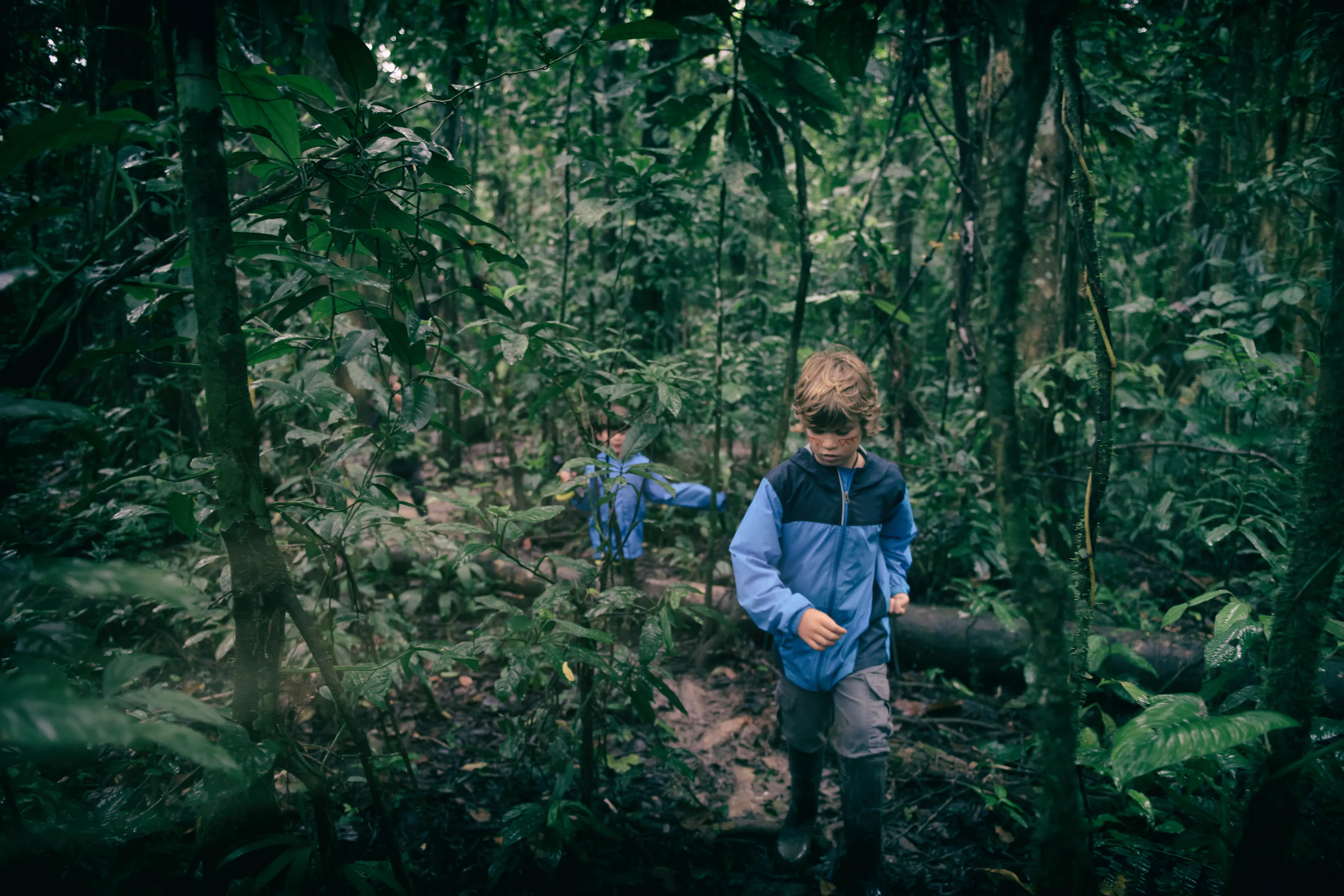 A family in rain gear walks along a forest boardwalk deep in the Peruvian Amazon, surrounded by dense greenery.
