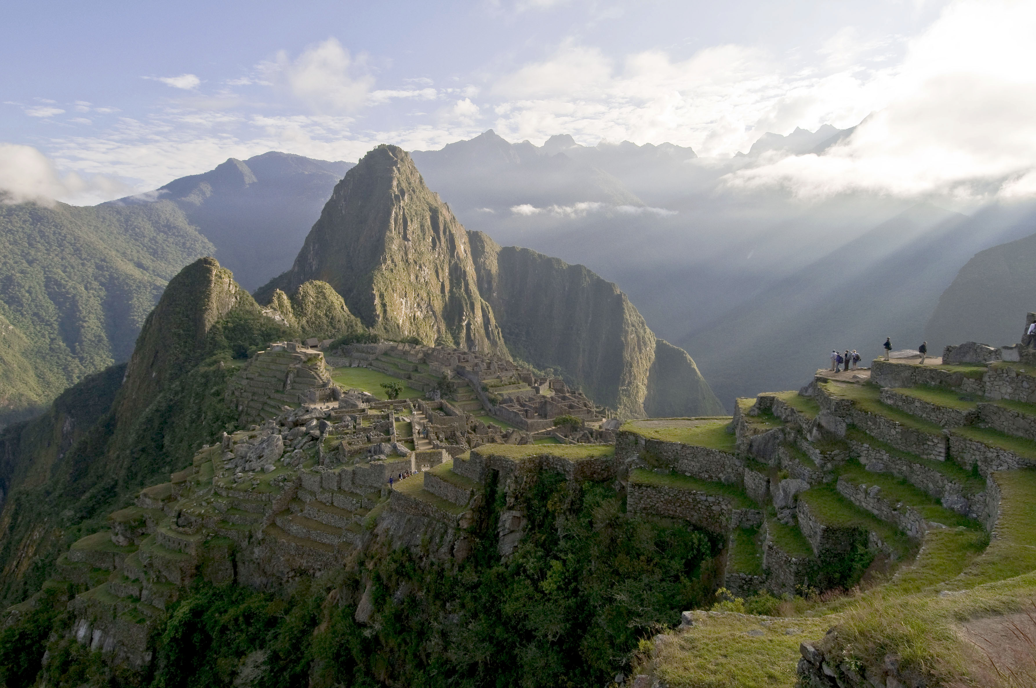 Sunbeams break through cloud over Machu Picchu, lighting the stone citadel and terraces above the valley.