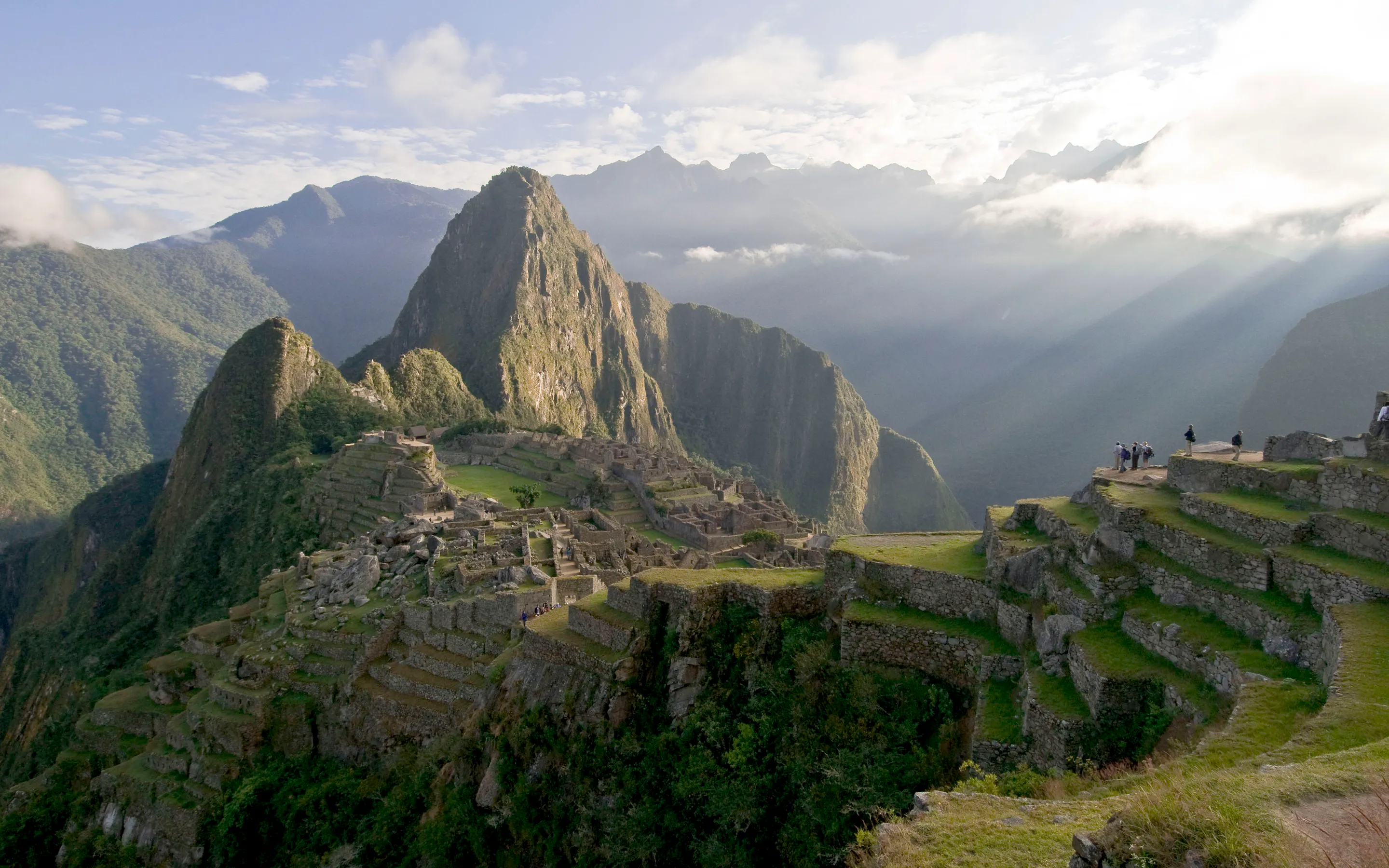 Sunbeams break through cloud over Machu Picchu, lighting the stone citadel and terraces above the valley.