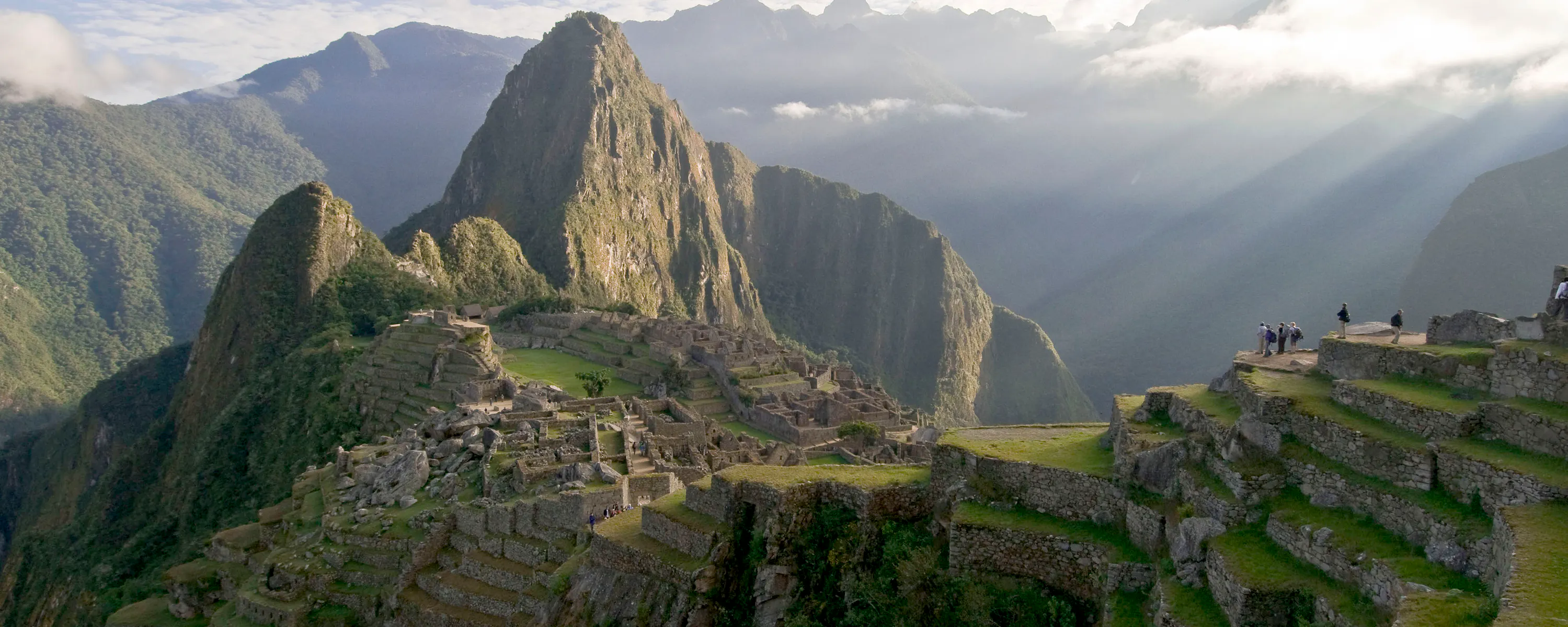 Sunbeams break through cloud over Machu Picchu, lighting the stone citadel and terraces above the valley.