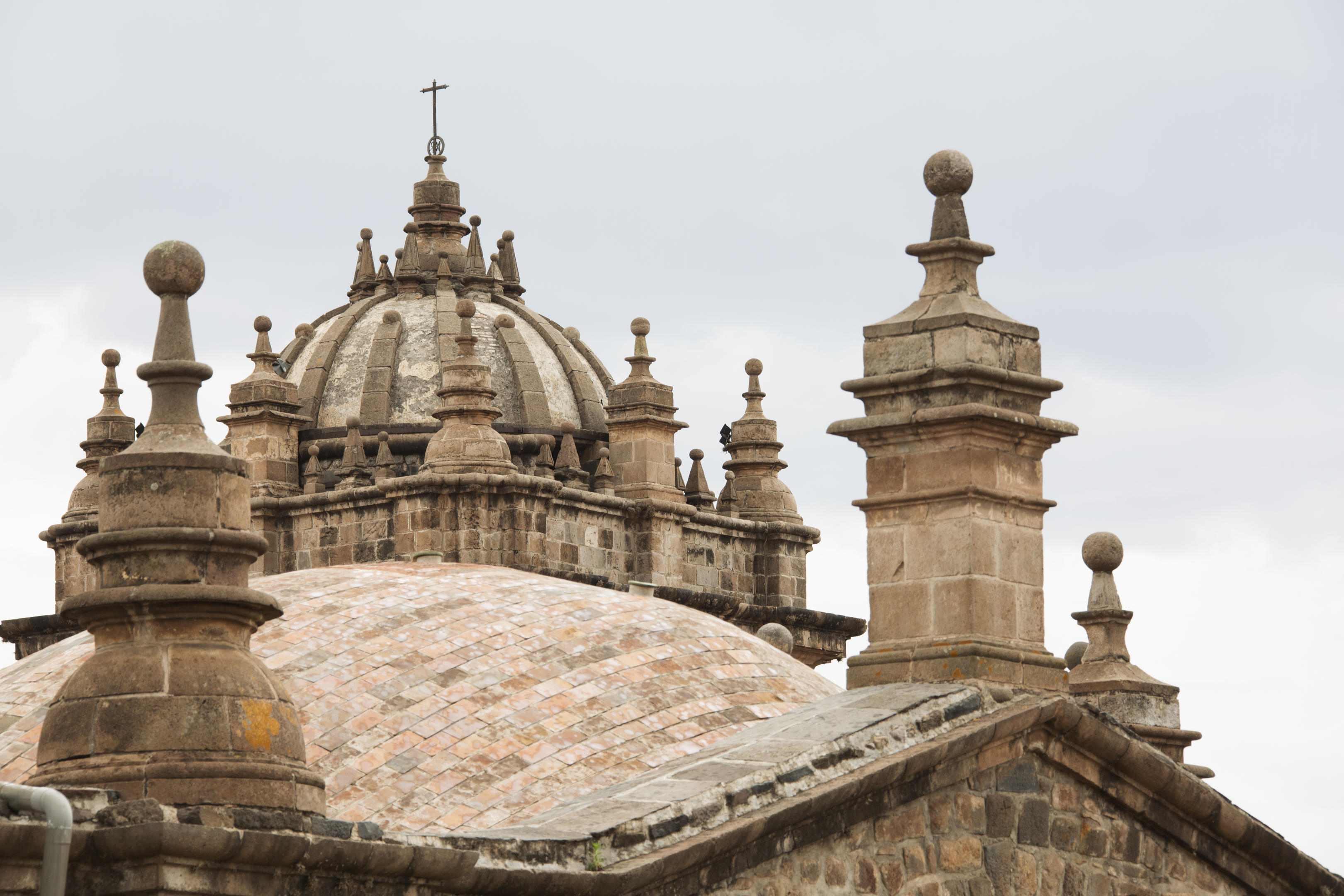 Weathered stone domes and cathedral spires rise against a gray sky in the historic center of Cusco, Peru.