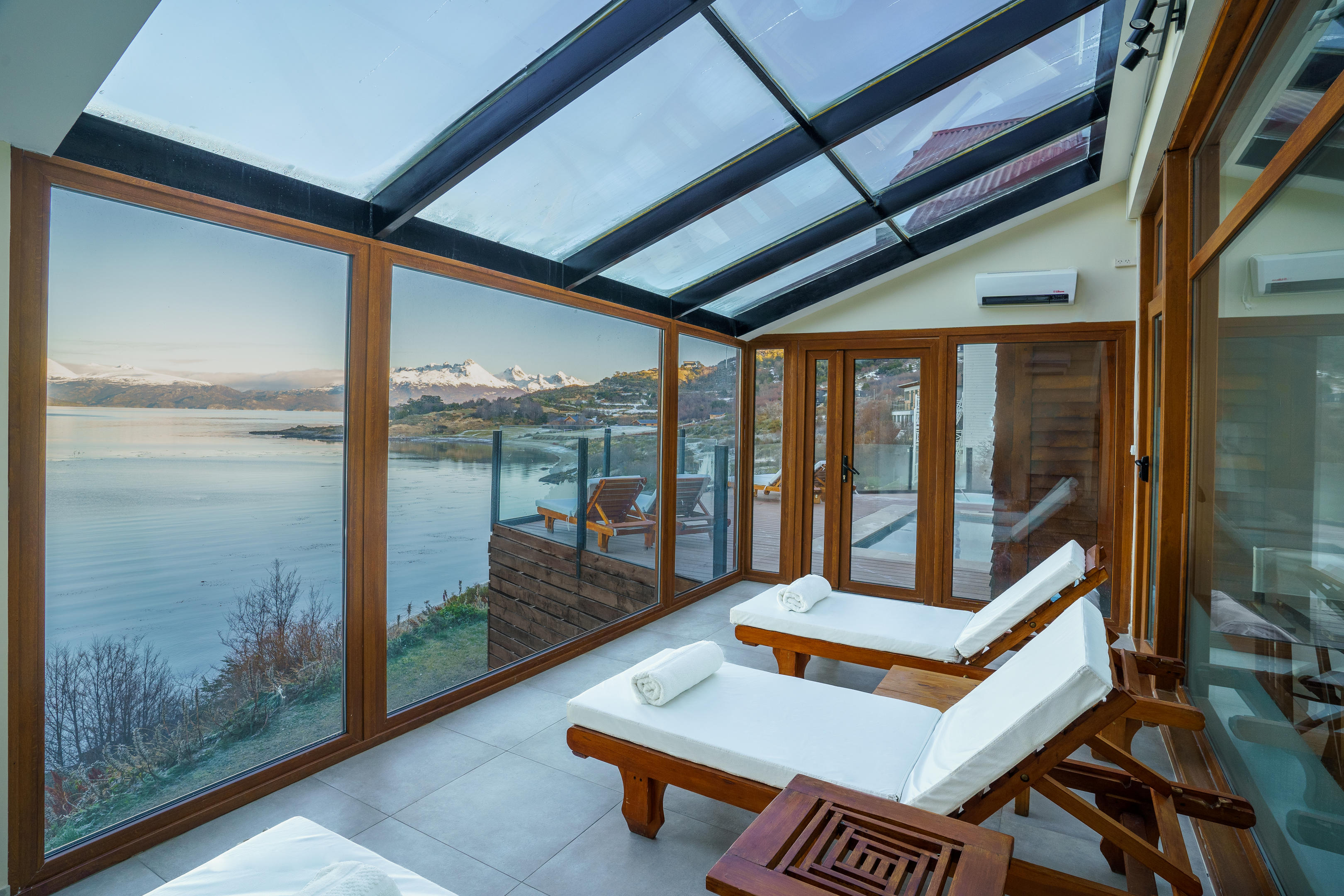 White loungers line a glass-walled spa terrace overlooking the Beagle Channel and snowy peaks near Ushuaia, Argentina.
