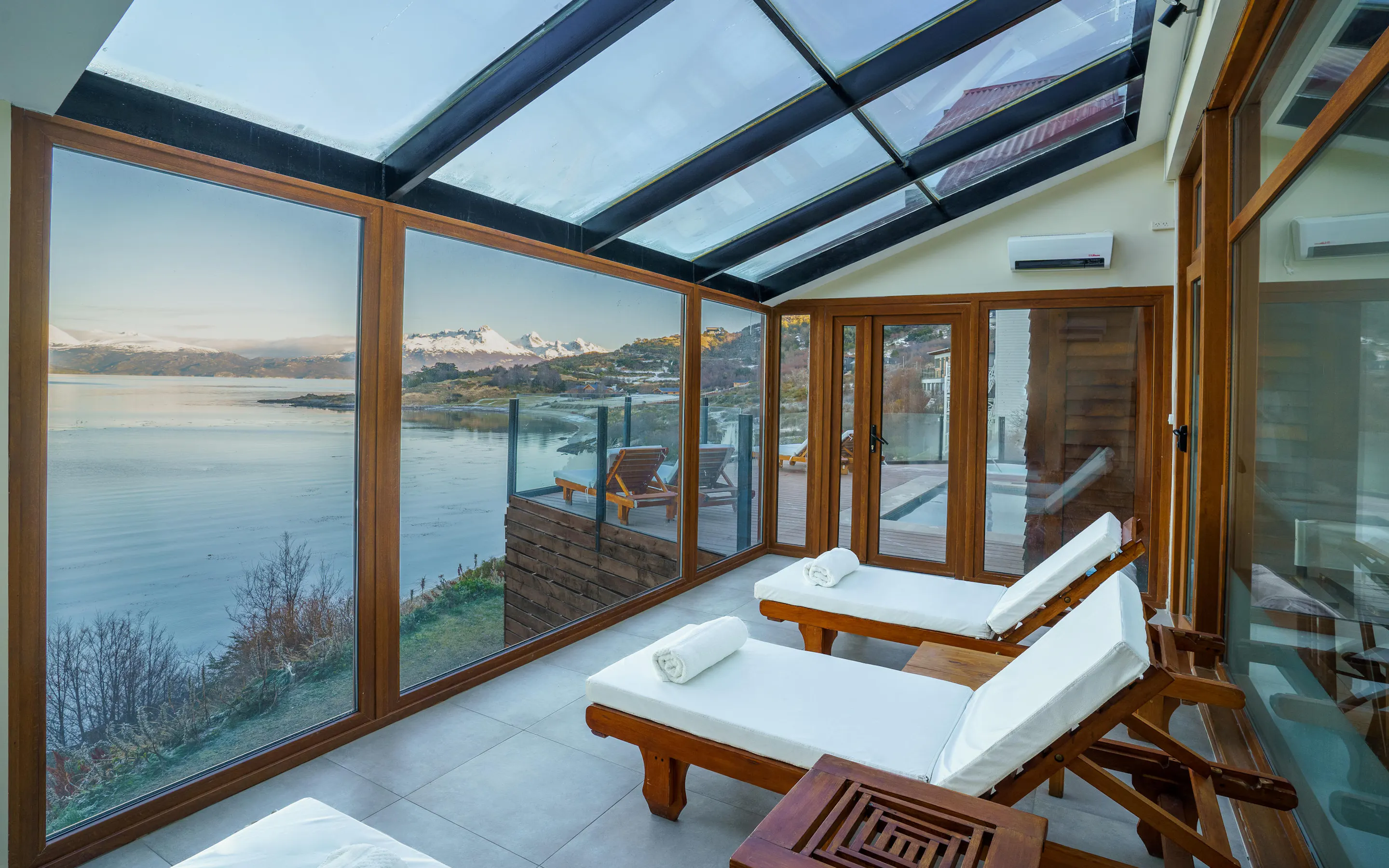 White loungers line a glass-walled spa terrace overlooking the Beagle Channel and snowy peaks near Ushuaia, Argentina.