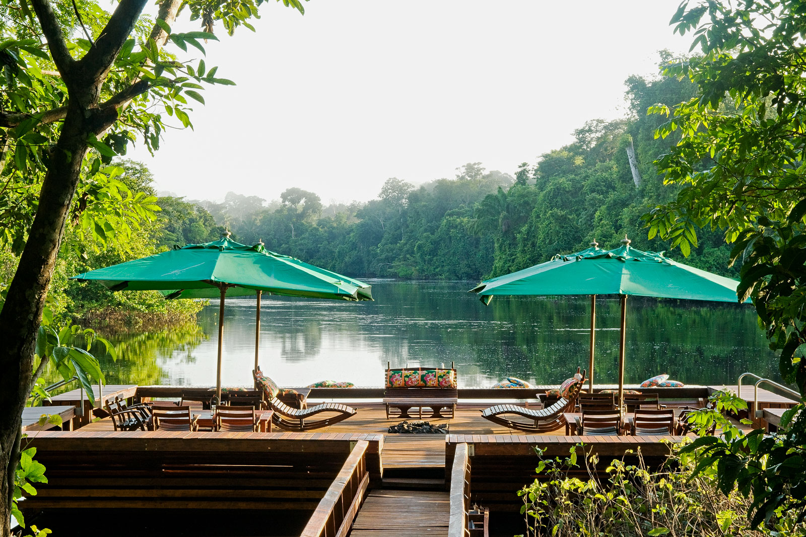 Wooden loungers and green umbrellas face the river from Cristalino Lodge, surrounded by dense Amazon forest.