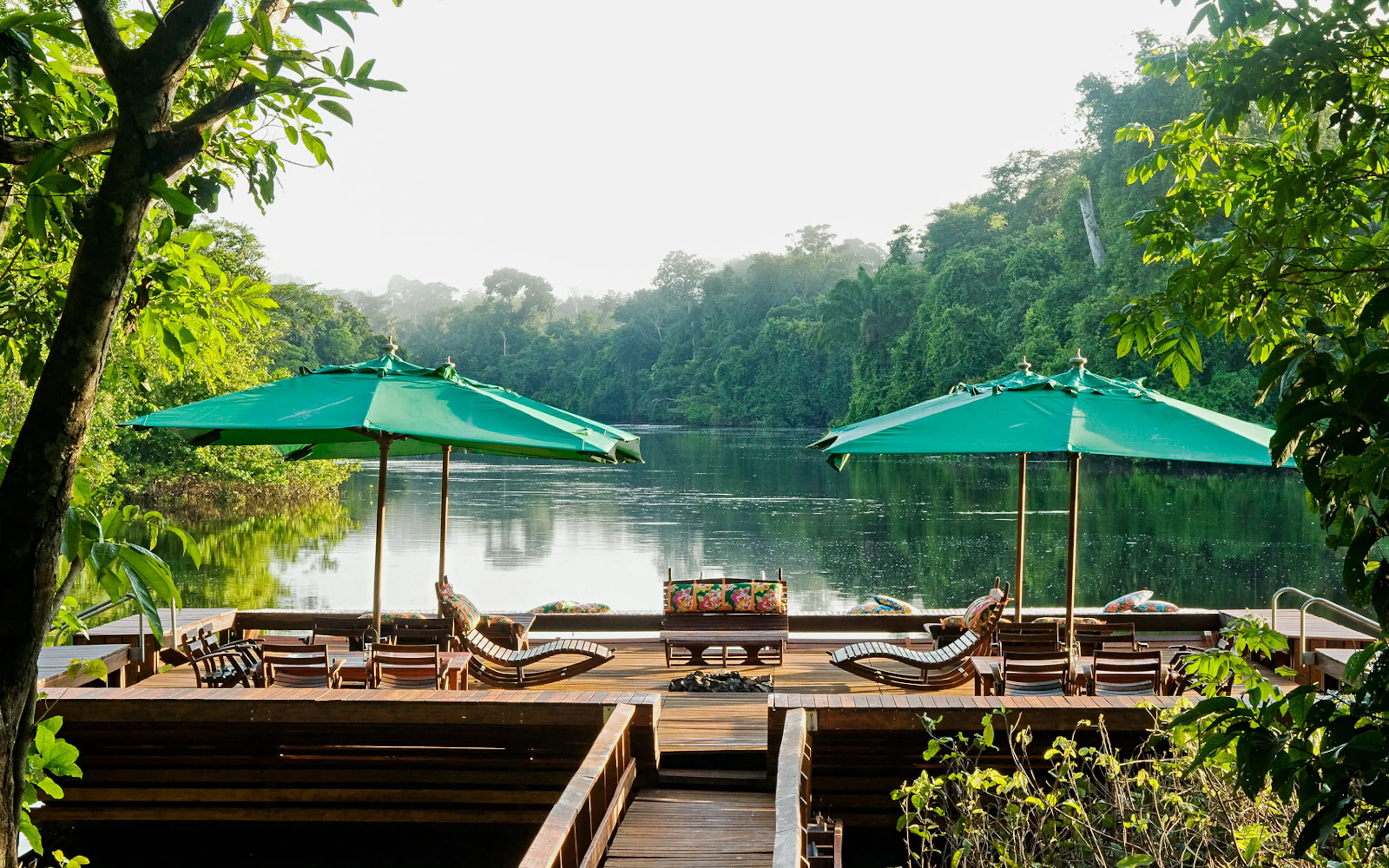 Wooden loungers and green umbrellas face the river from Cristalino Lodge, surrounded by dense Amazon forest.