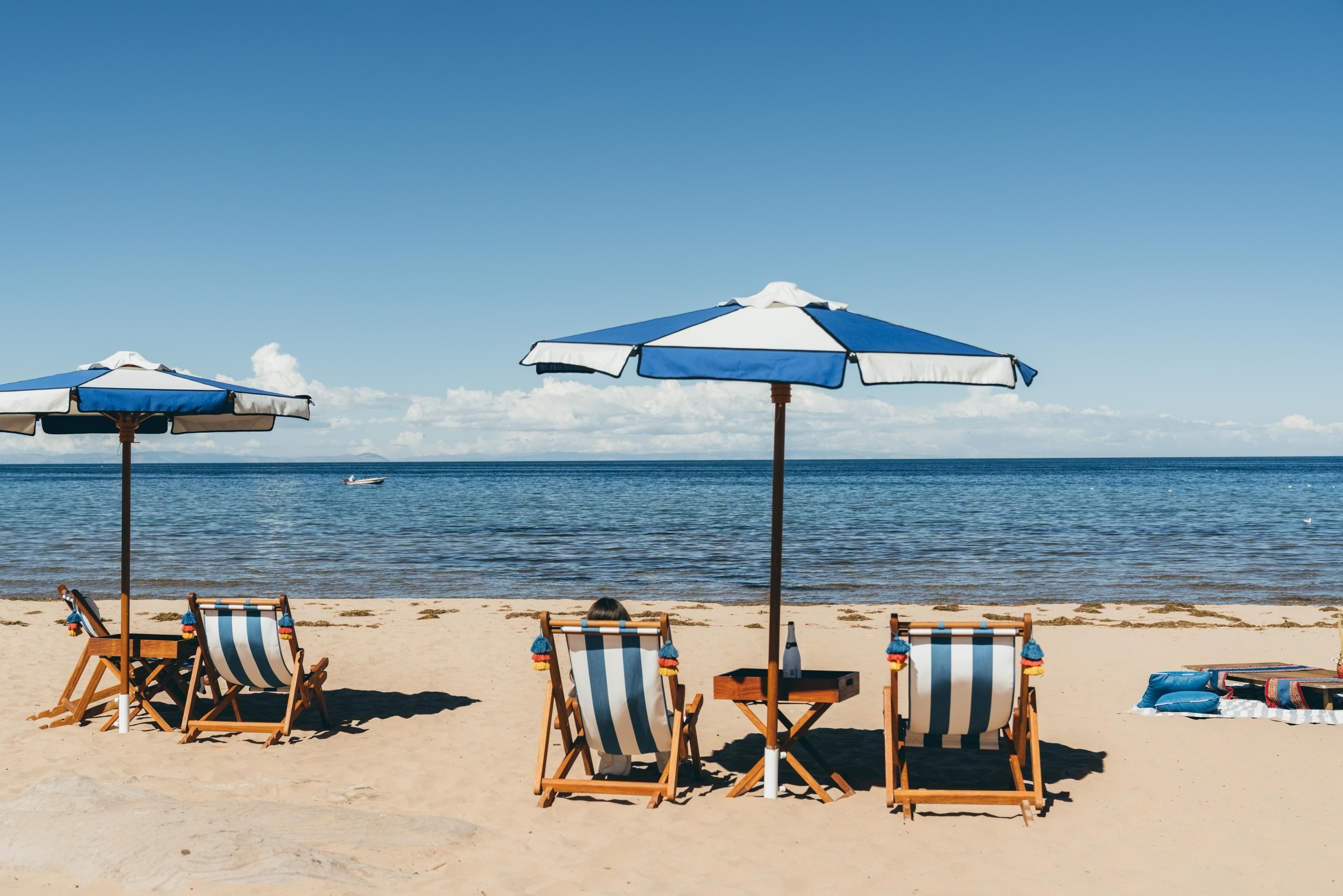 Striped beach chairs and blue umbrellas line the shore at Collata Beach, facing the vast calm waters of Lake Titicaca.