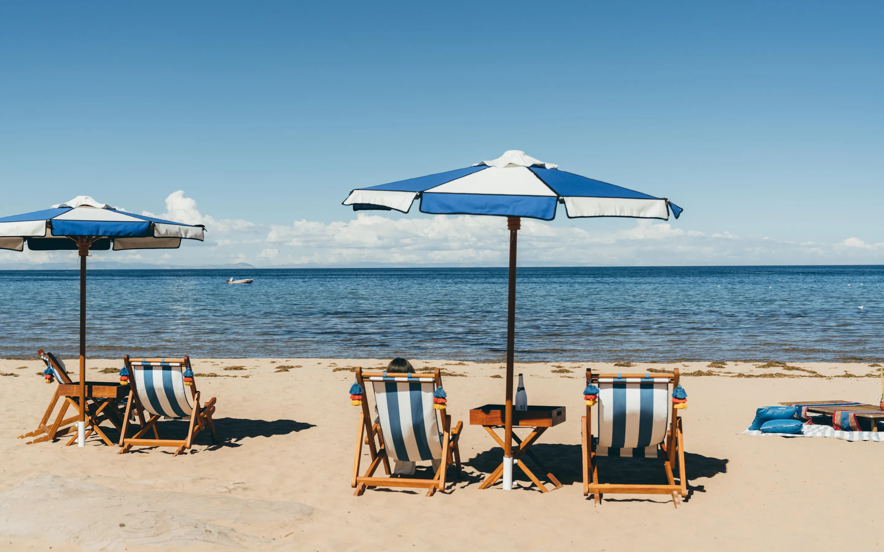 Striped beach chairs and blue umbrellas line the shore at Collata Beach, facing the vast calm waters of Lake Titicaca.