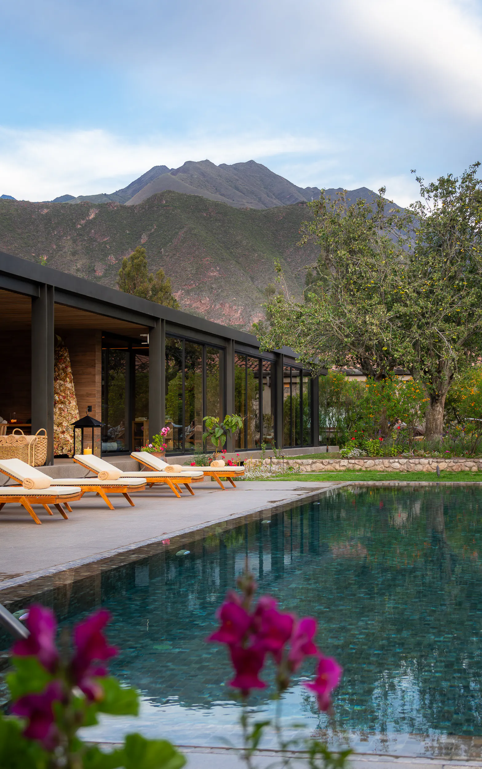 A serene pool reflects the mountains at Sol y Luna, where bright flowers and loungers frame the Sacred Valley view.