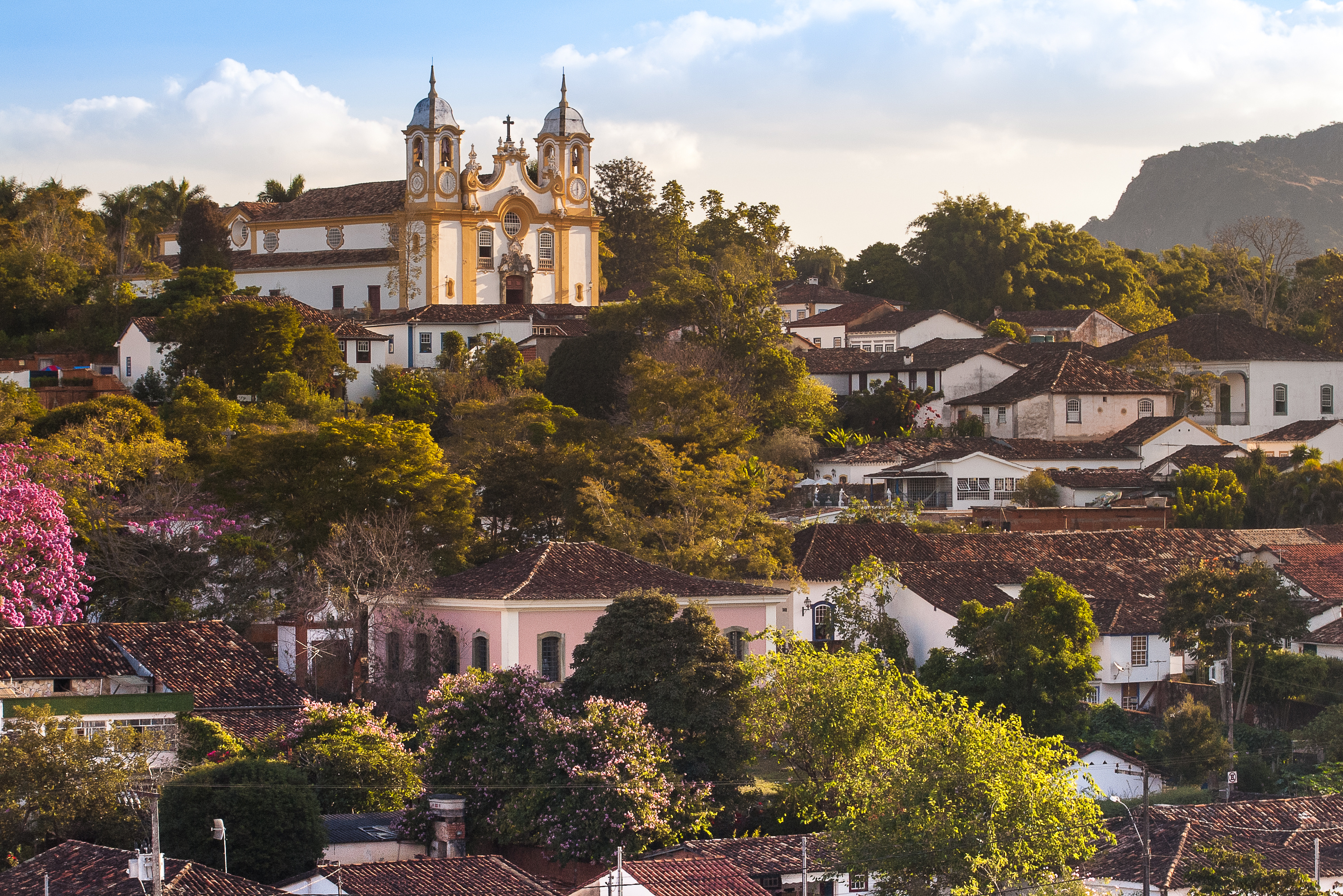 Historic Tiradentes climbs a Minas Gerais hillside, with church towers, tiled roofs, and soft evening light.