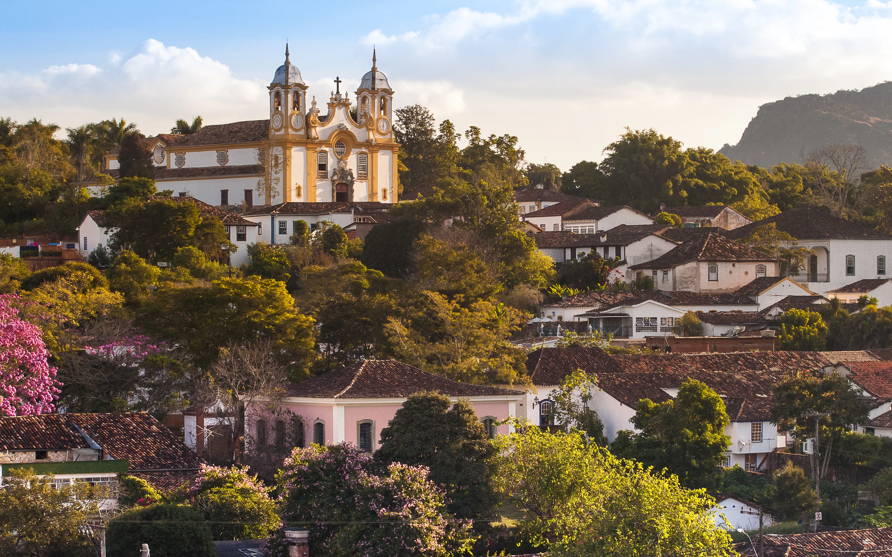 Historic Tiradentes climbs a Minas Gerais hillside, with church towers, tiled roofs, and soft evening light.