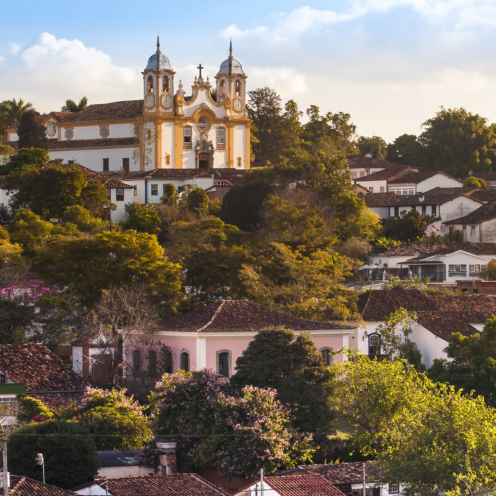 Historic Tiradentes climbs a Minas Gerais hillside, with church towers, tiled roofs, and soft evening light.