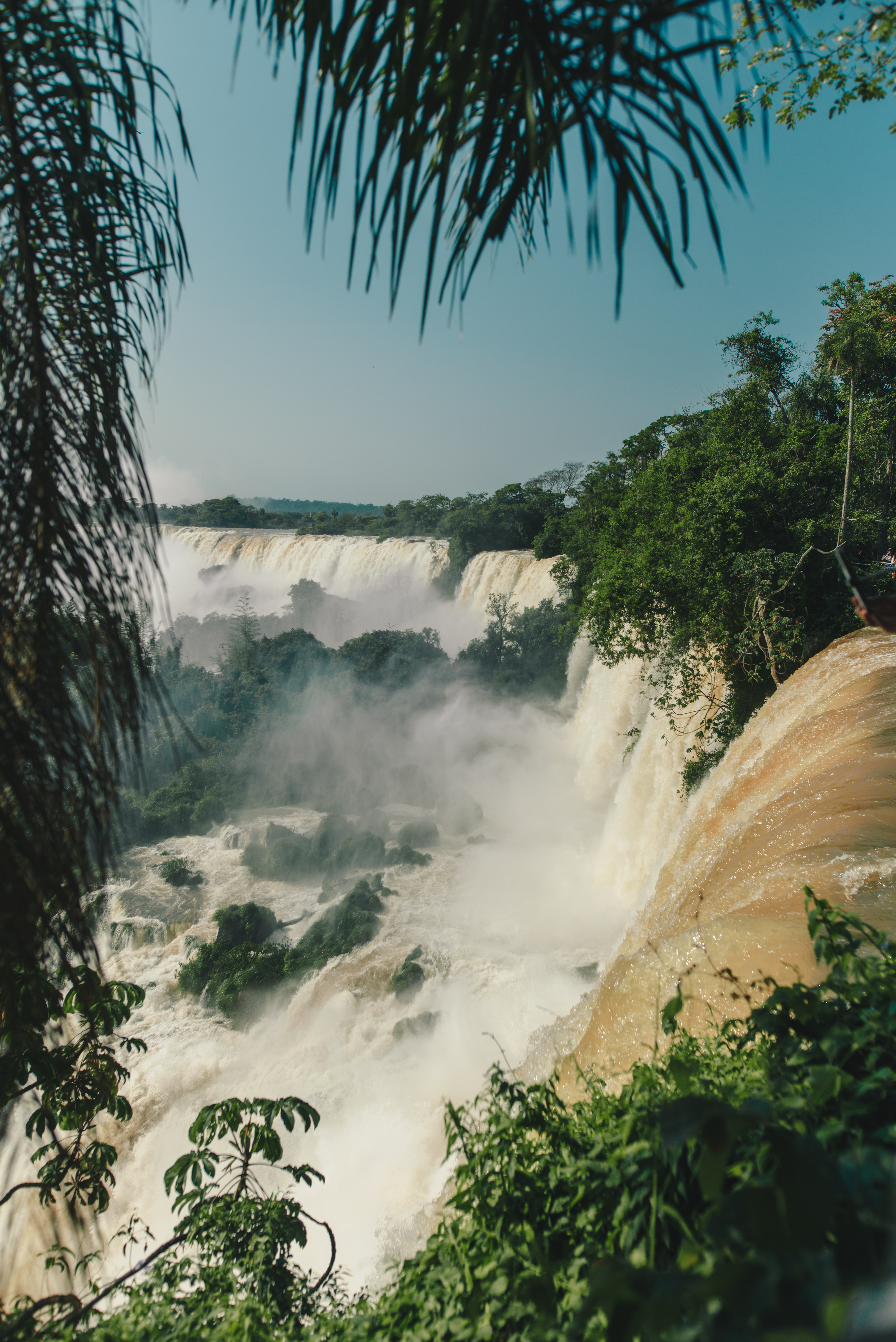 Broad waterfalls pour through lush forest at Iguazu Falls, with white mist rising above the rocky river below.