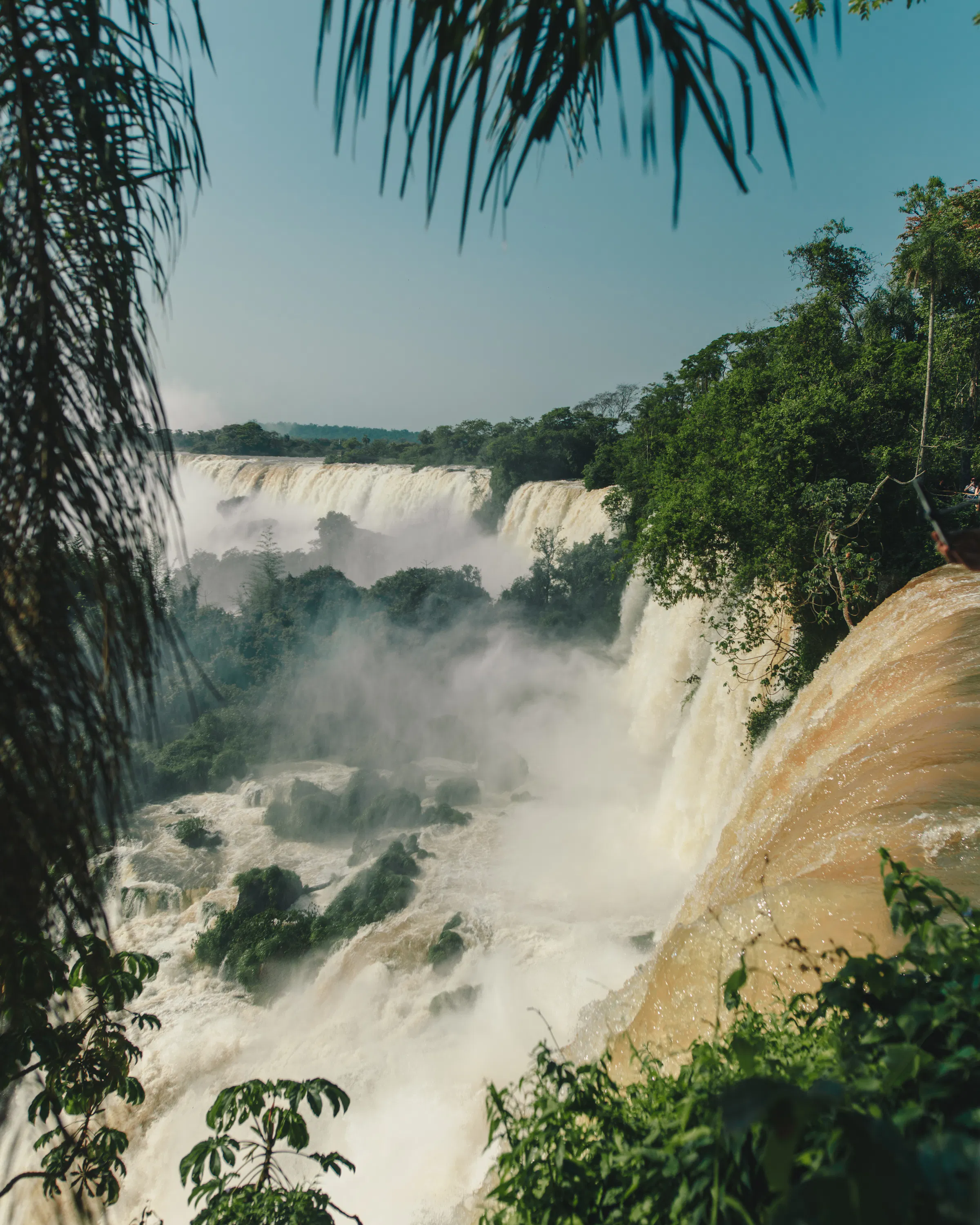 Broad waterfalls pour through lush forest at Iguazu Falls, with white mist rising above the rocky river below.
