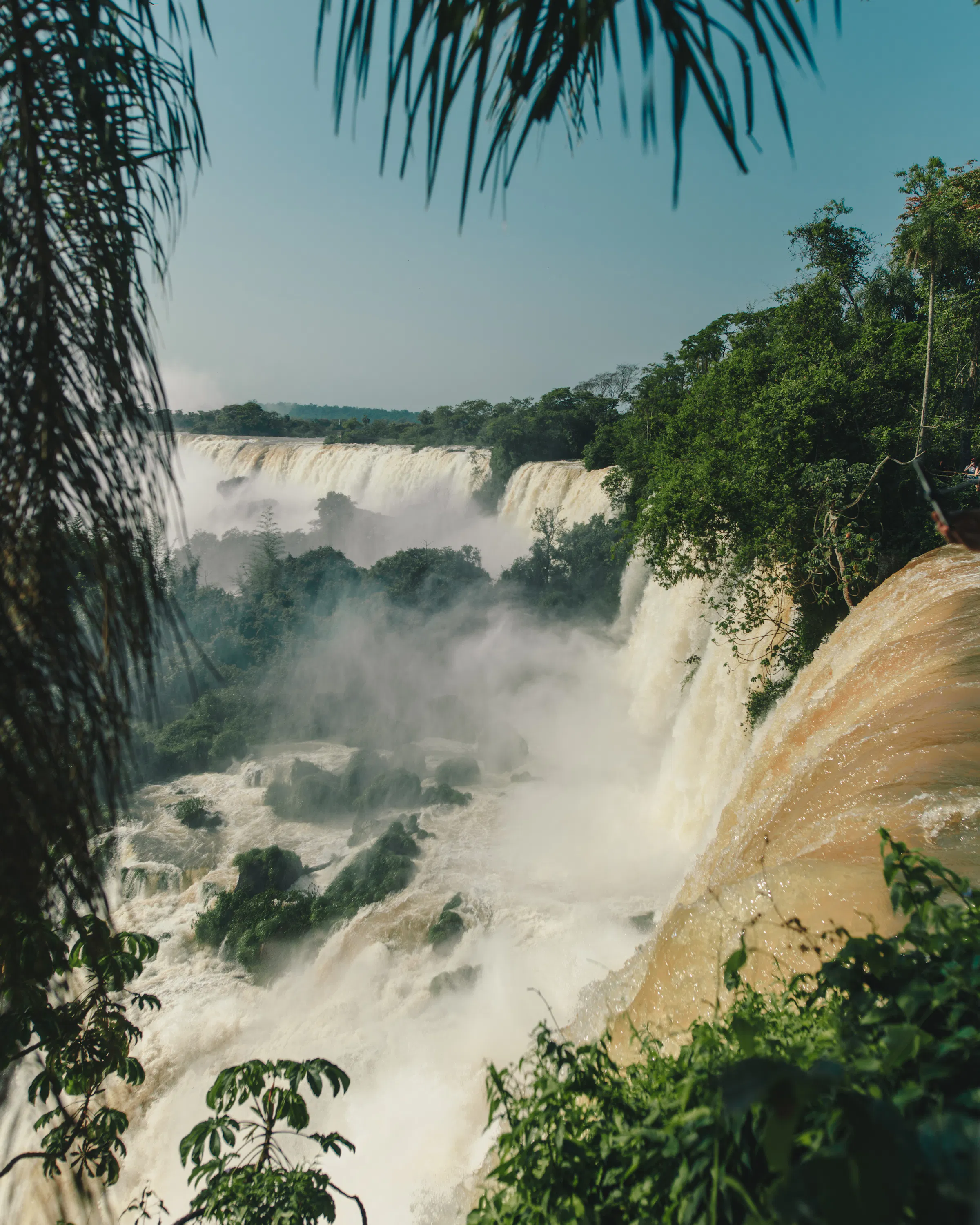 Broad waterfalls pour through lush forest at Iguazu Falls, with white mist rising above the rocky river below.