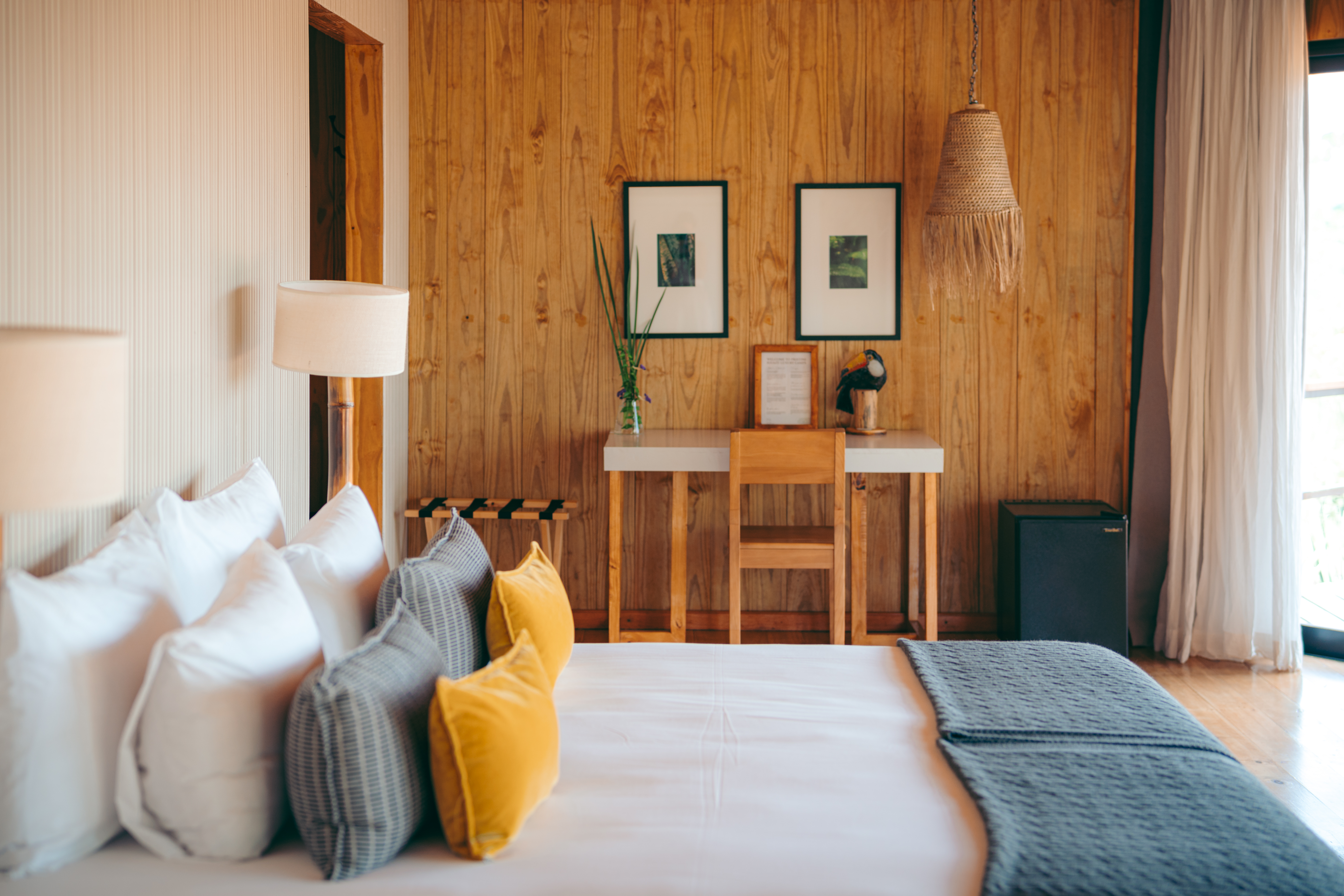 A neatly styled bedroom with wood-paneled walls, framed art, and a daybed opens toward the forest at Pristine Iguazu.