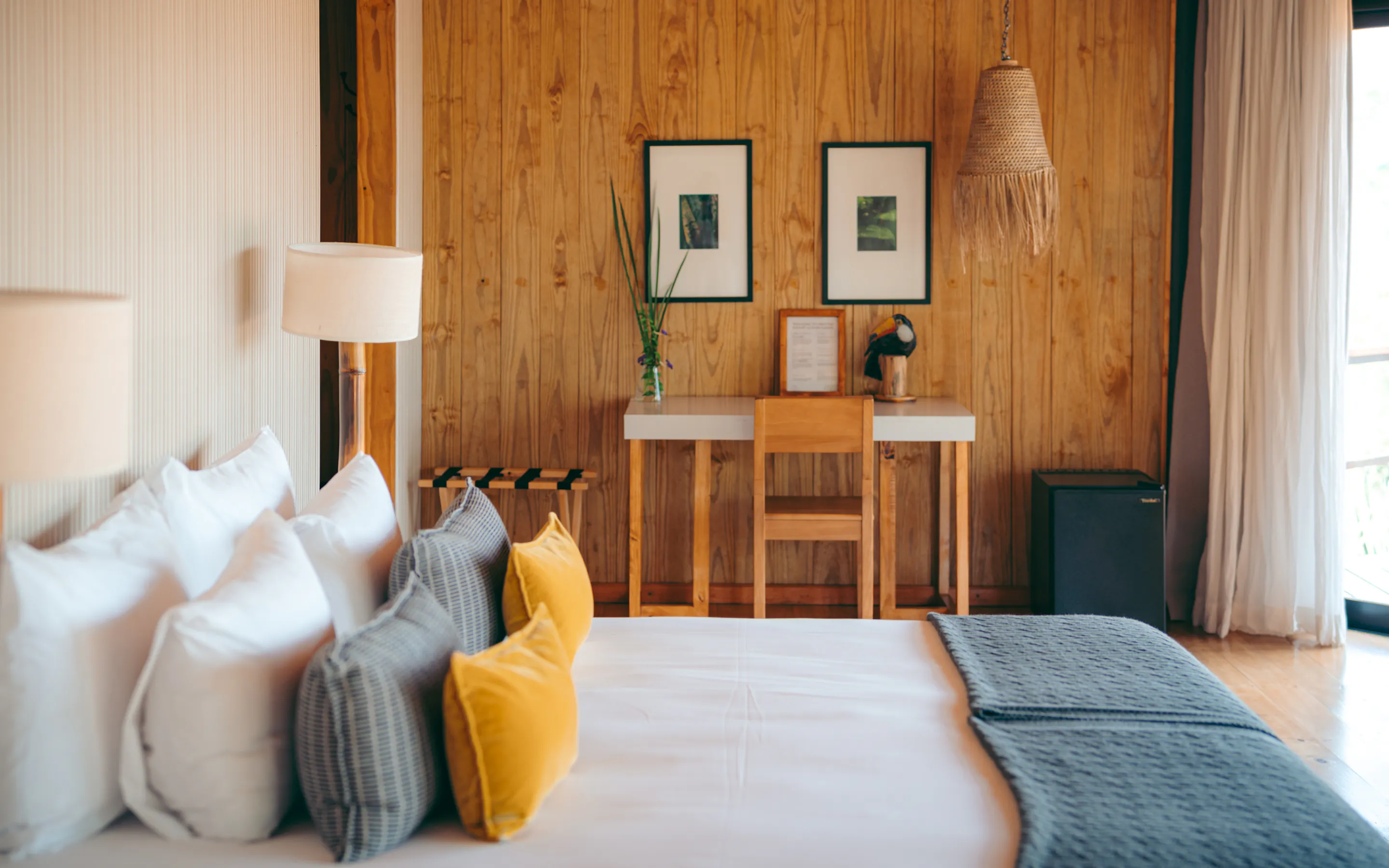A neatly styled bedroom with wood-paneled walls, framed art, and a daybed opens toward the forest at Pristine Iguazu.
