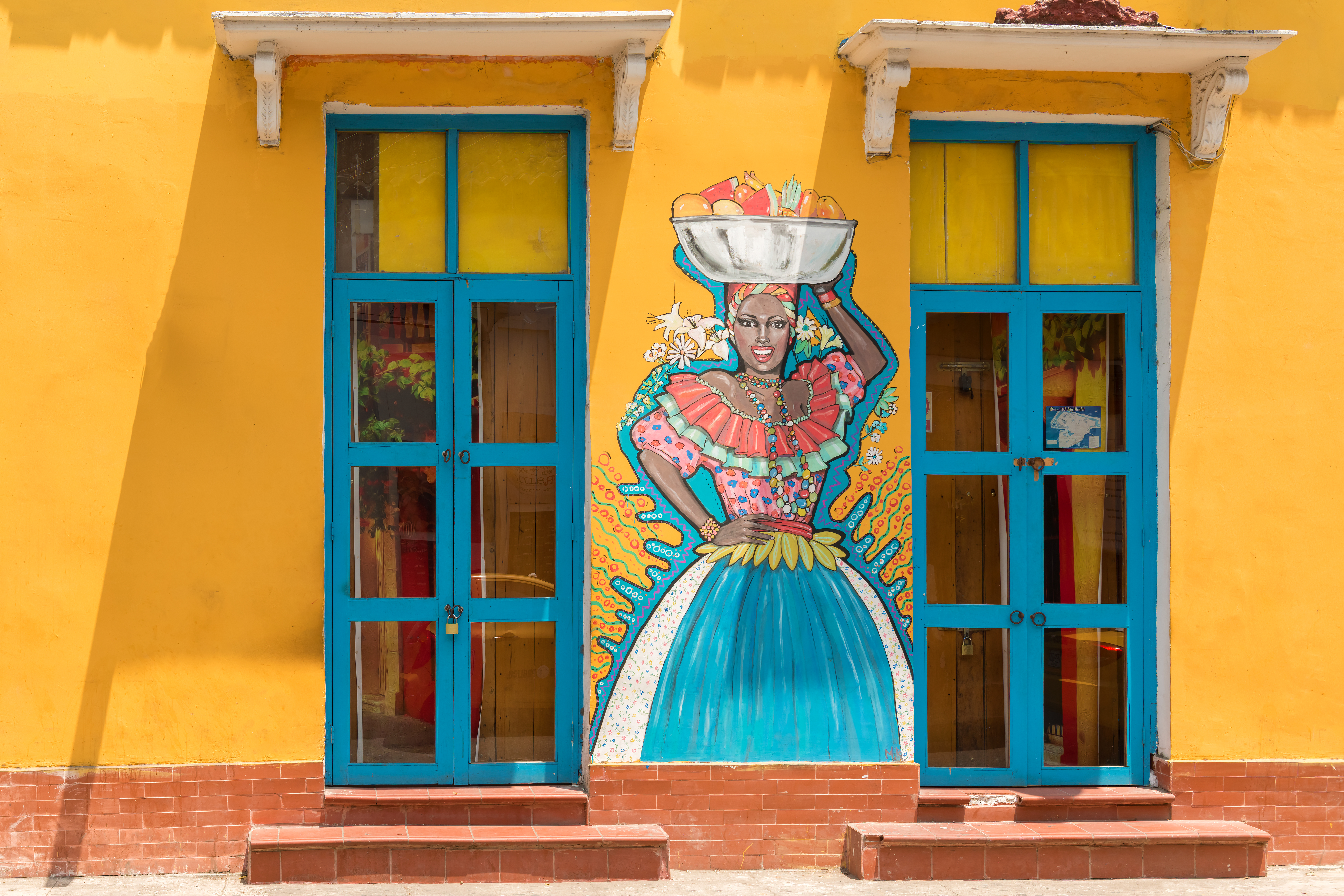 A painted doorway framed by bright yellow walls features a colorful street-art figure in Cartagena's Getsemani district.