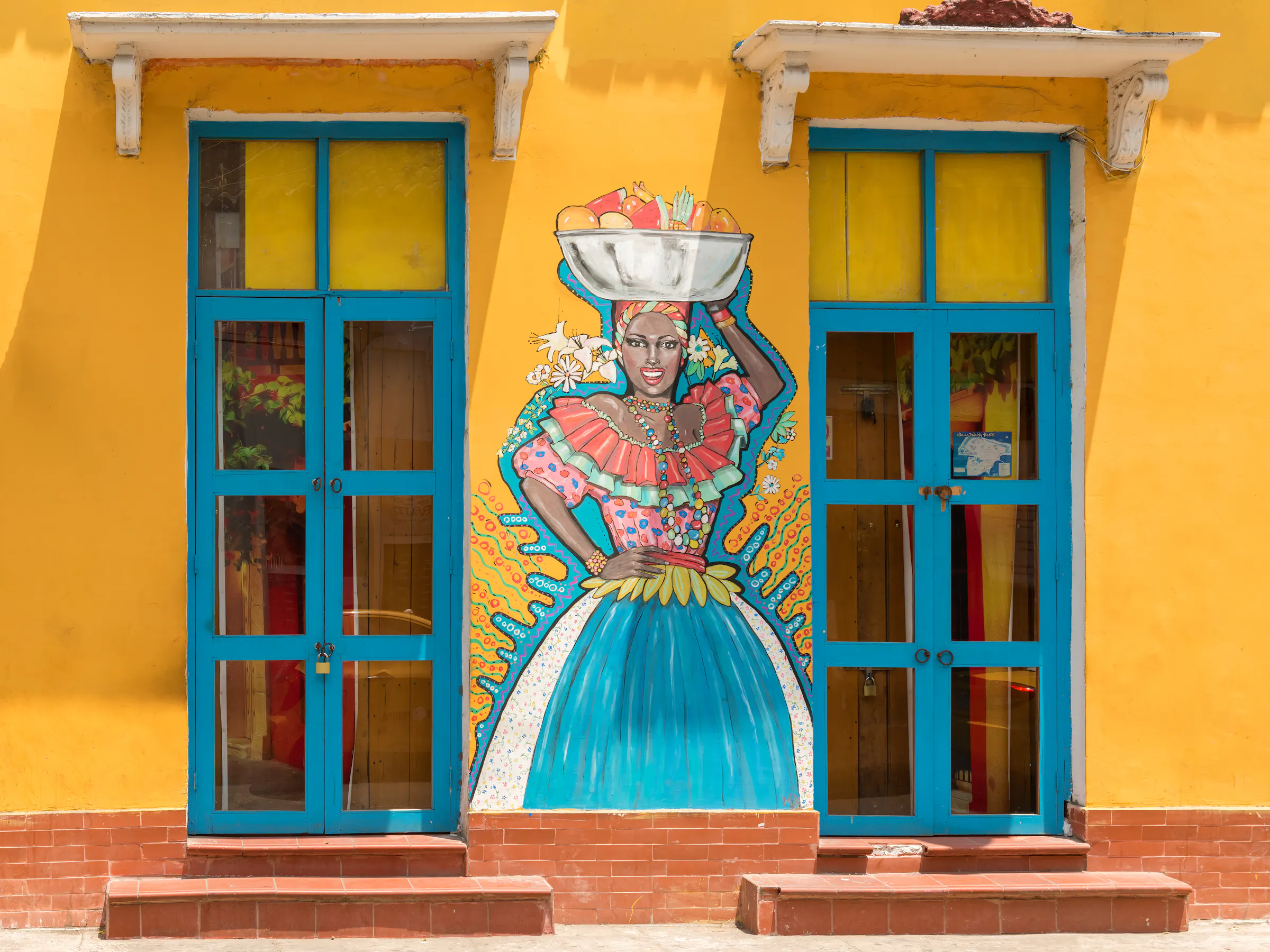 A painted doorway framed by bright yellow walls features a colorful street-art figure in Cartagena's Getsemani district.