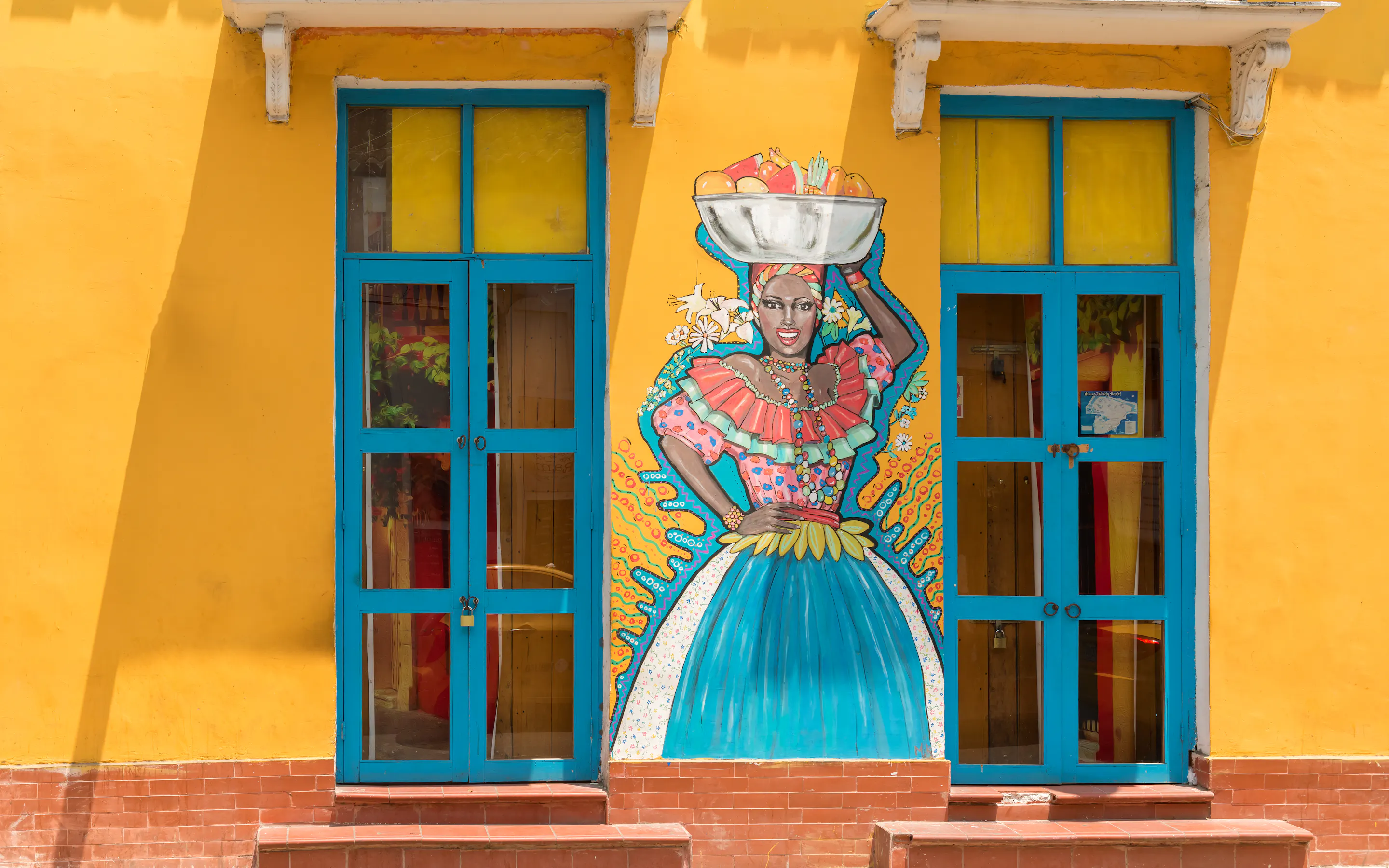 A painted doorway framed by bright yellow walls features a colorful street-art figure in Cartagena's Getsemani district.