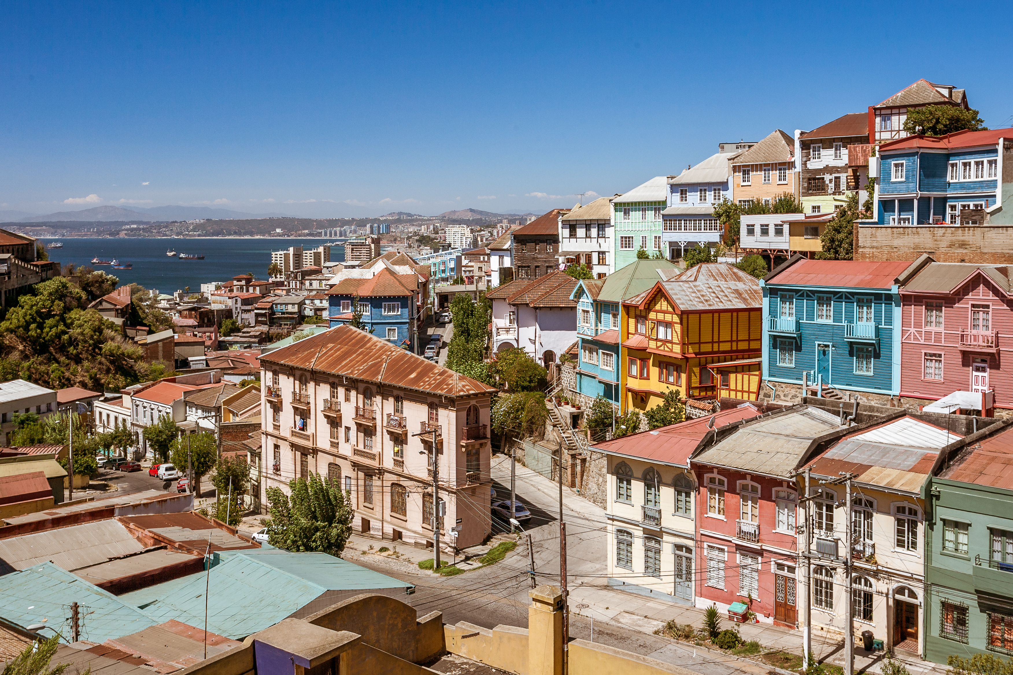 Colorful hillside houses stack above the harbor in Valparaiso, with steep streets and bright facades under clear light.