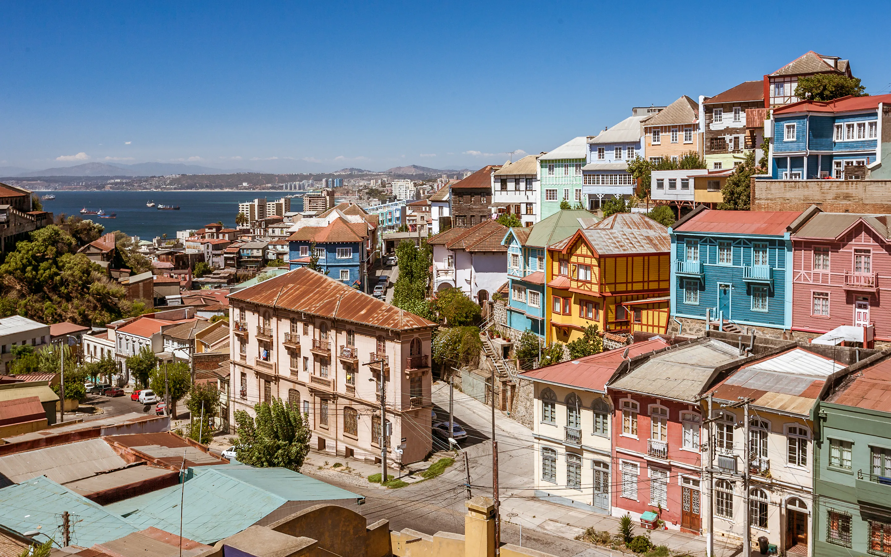 Colorful hillside houses stack above the harbor in Valparaiso, with steep streets and bright facades under clear light.
