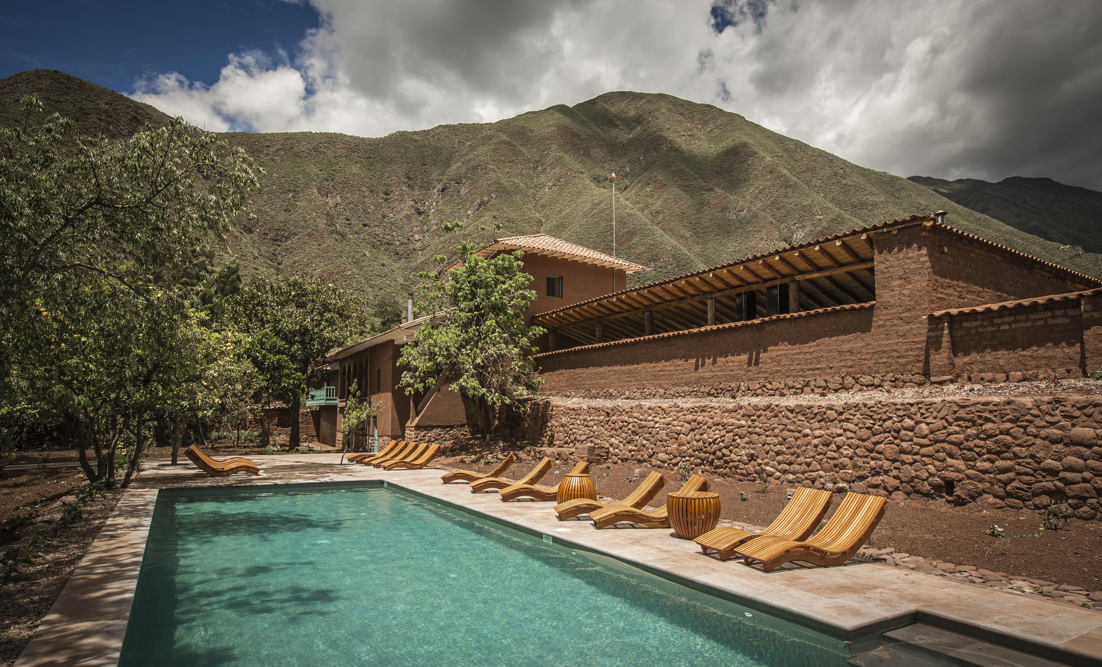A long pool and row of loungers sit beneath stone walls and mountains at Explora Valle Sagrado in Peru's Andes.