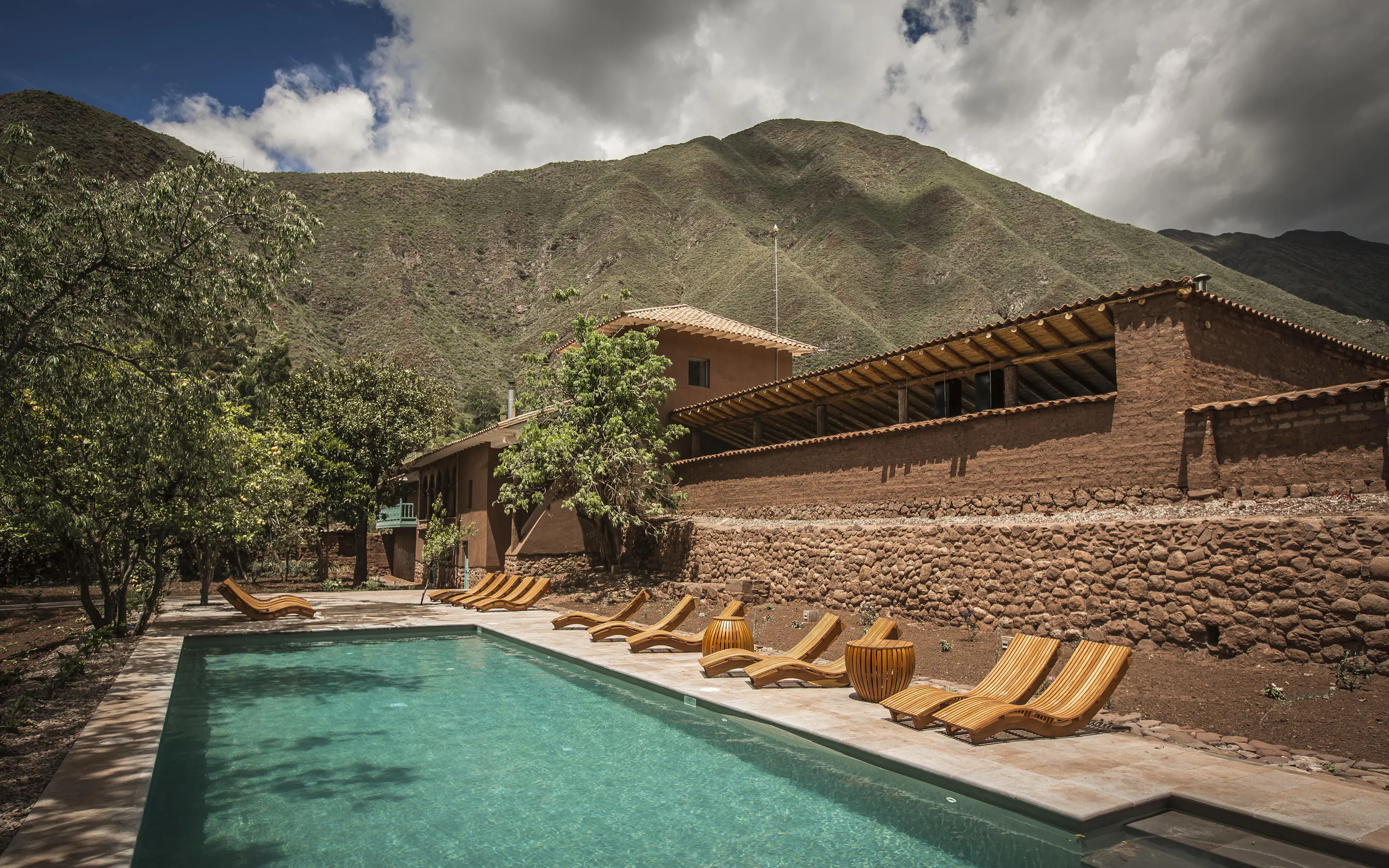 A long pool and row of loungers sit beneath stone walls and mountains at Explora Valle Sagrado in Peru's Andes.