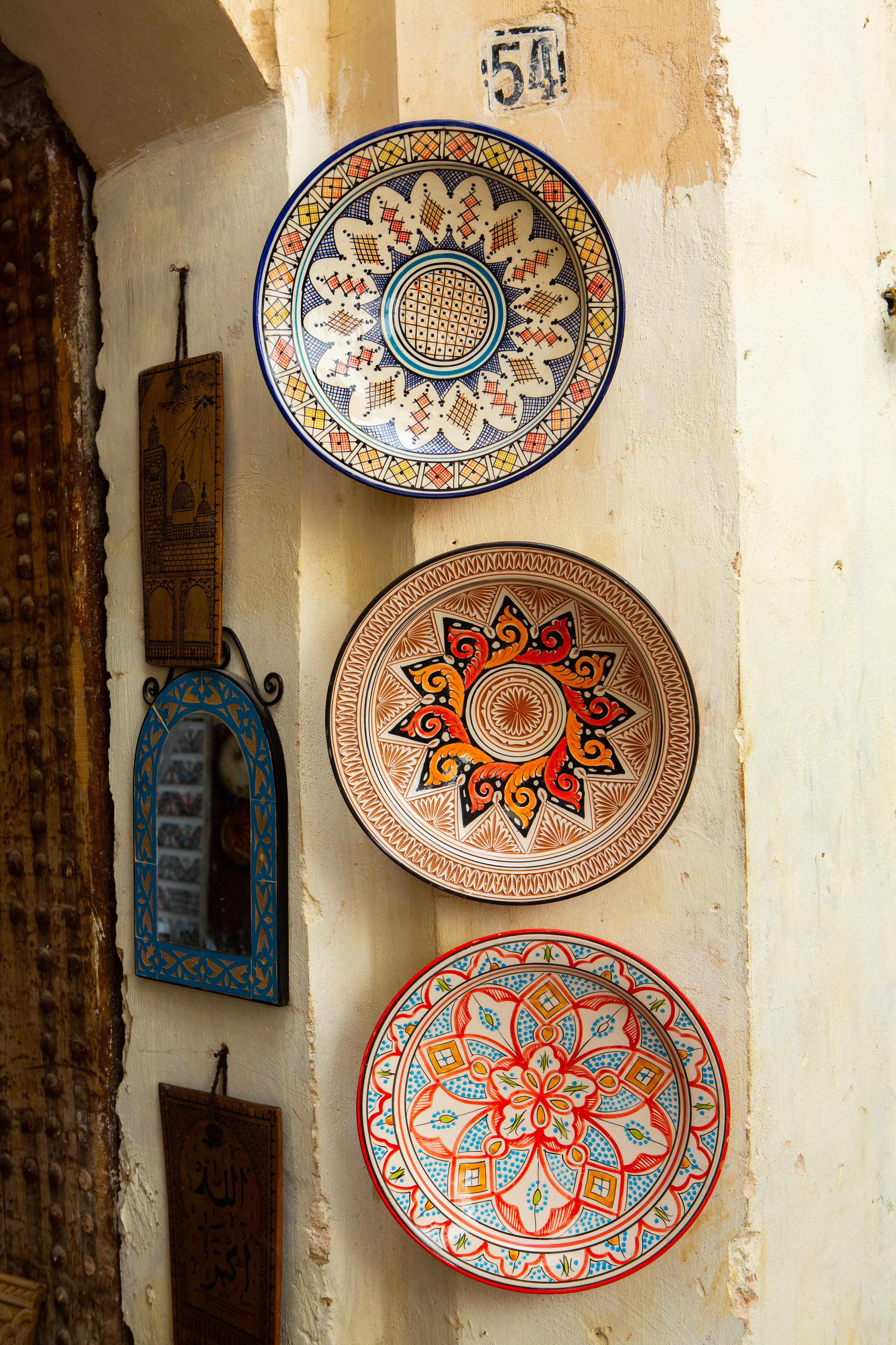 Colorful hand-painted ceramic plates displayed on a wall in a narrow alley.