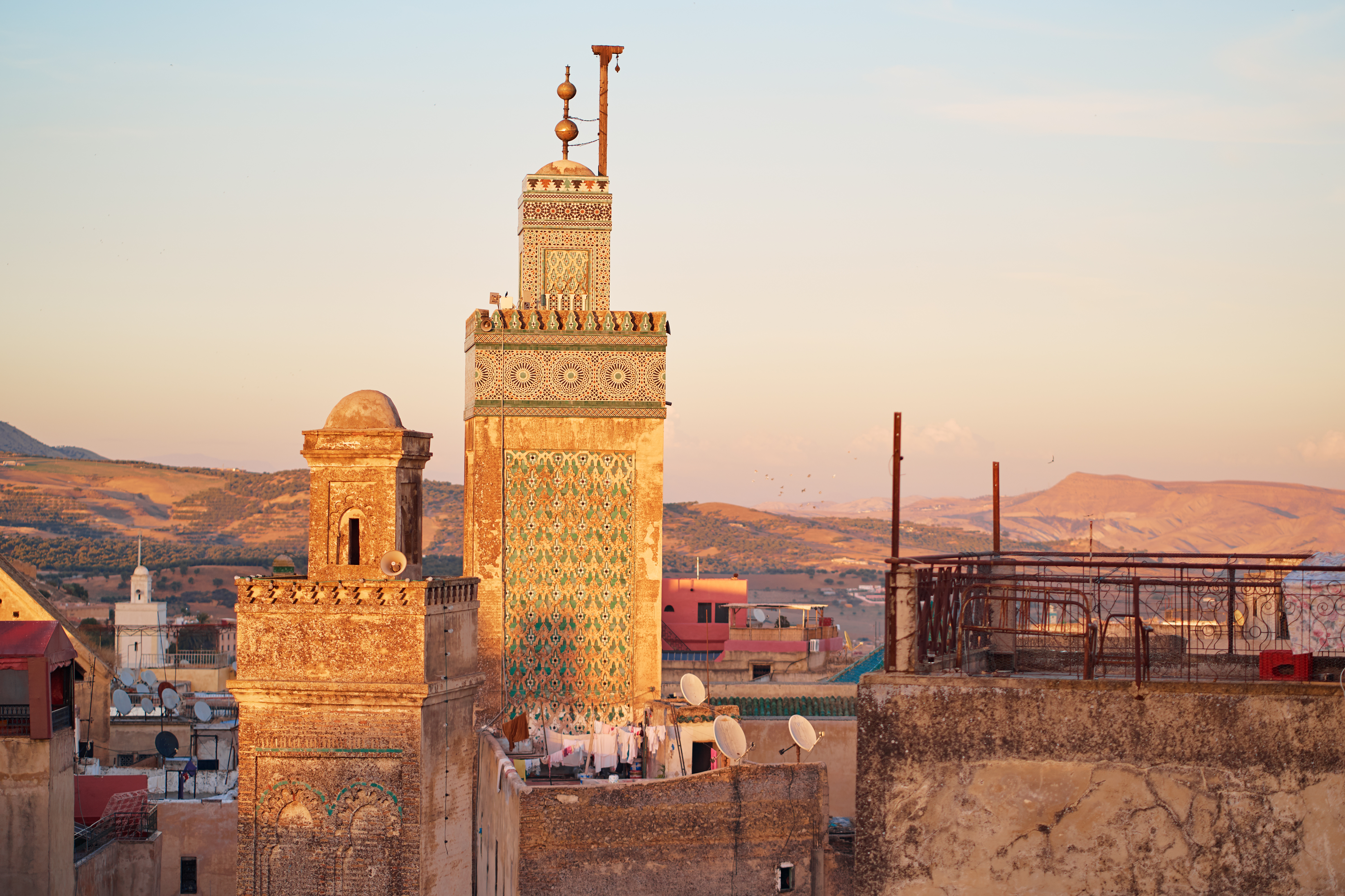Ornate minaret and historic buildings of Fes glowing in warm evening light.