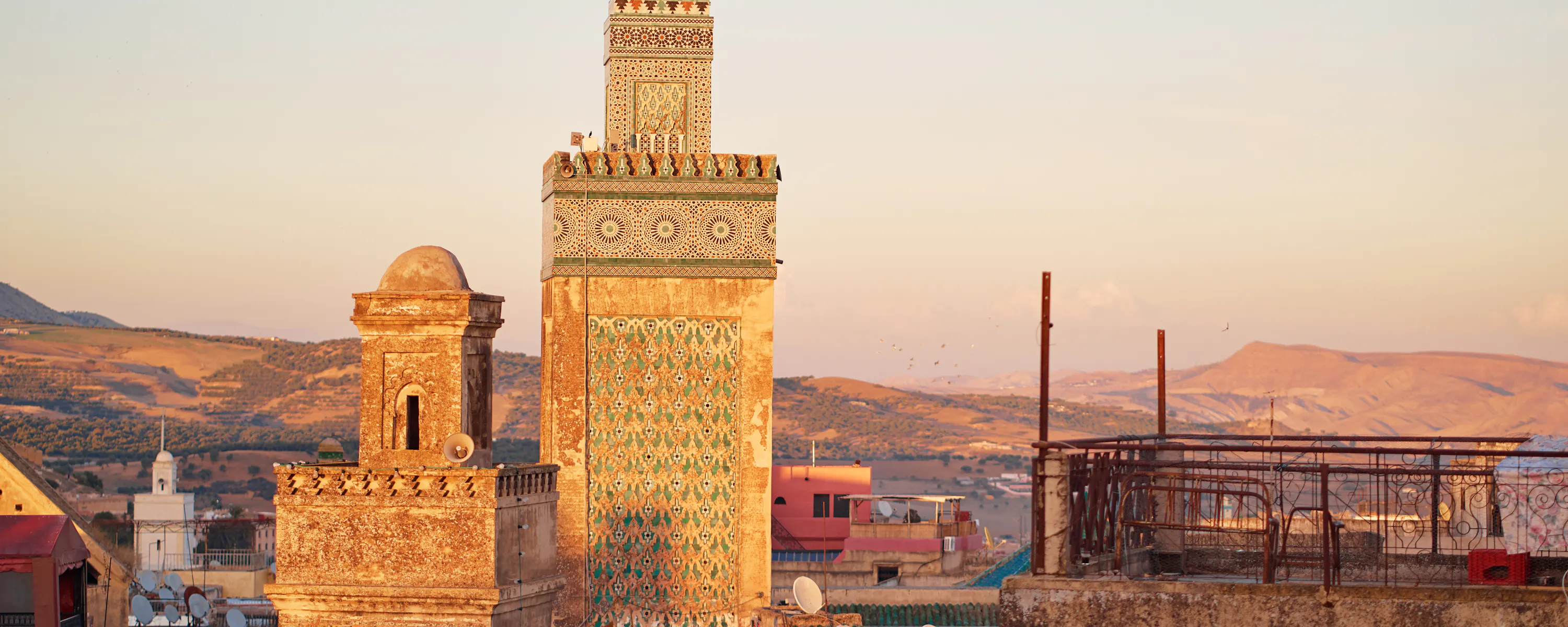 Ornate minaret and historic buildings of Fes glowing in warm evening light.