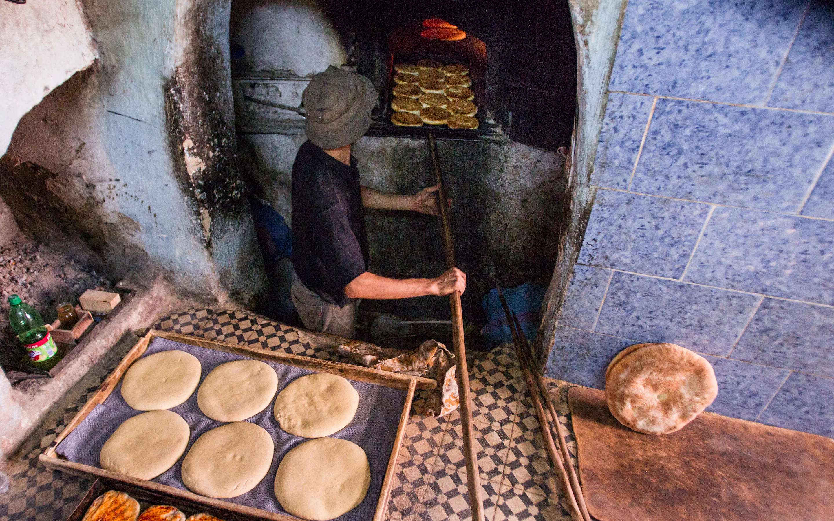 Man placing rounds of dough into a traditional stone oven inside a rustic bakery.
