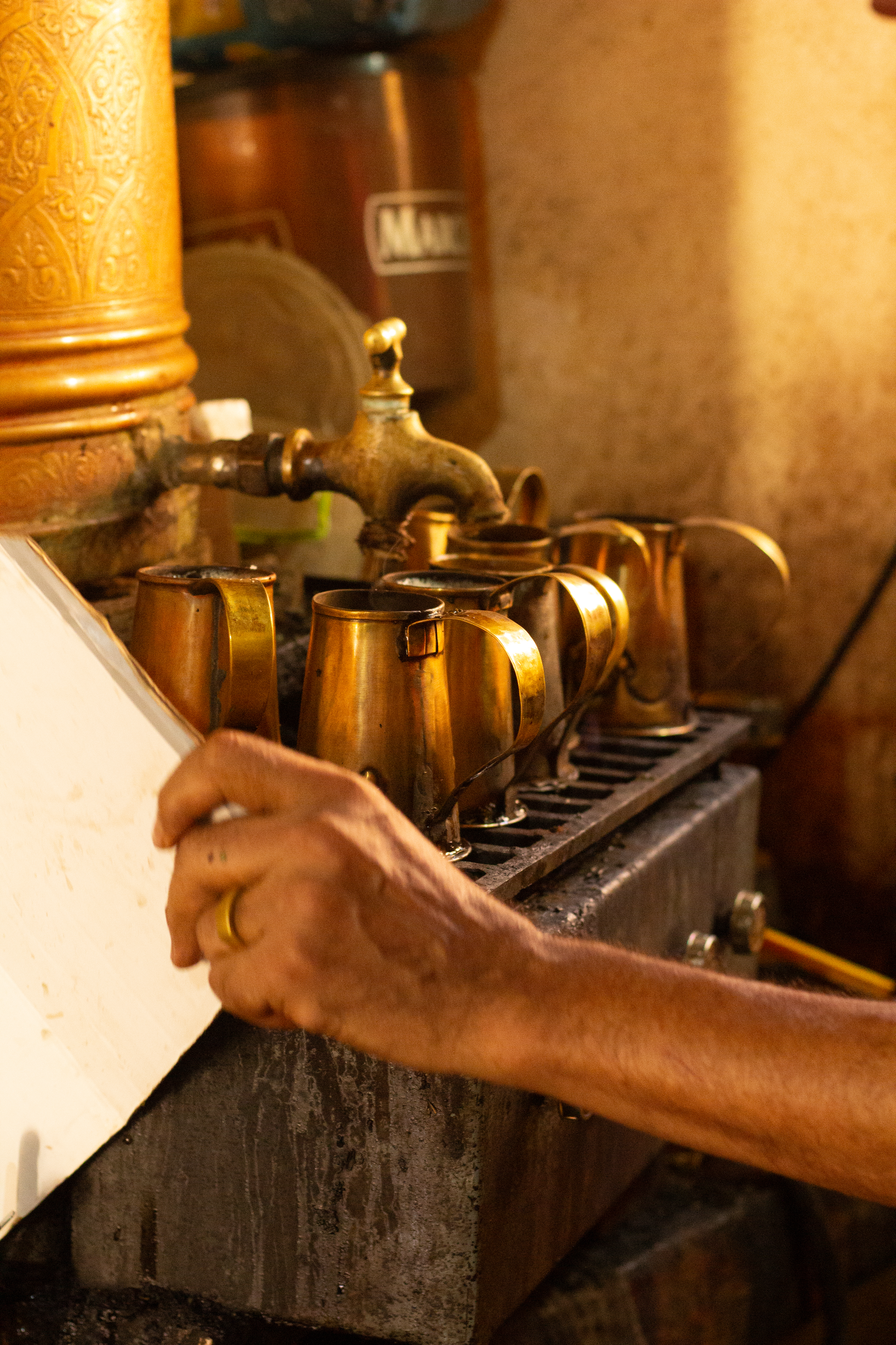 Close-up of tea being poured from a brass tap into small metal cups.