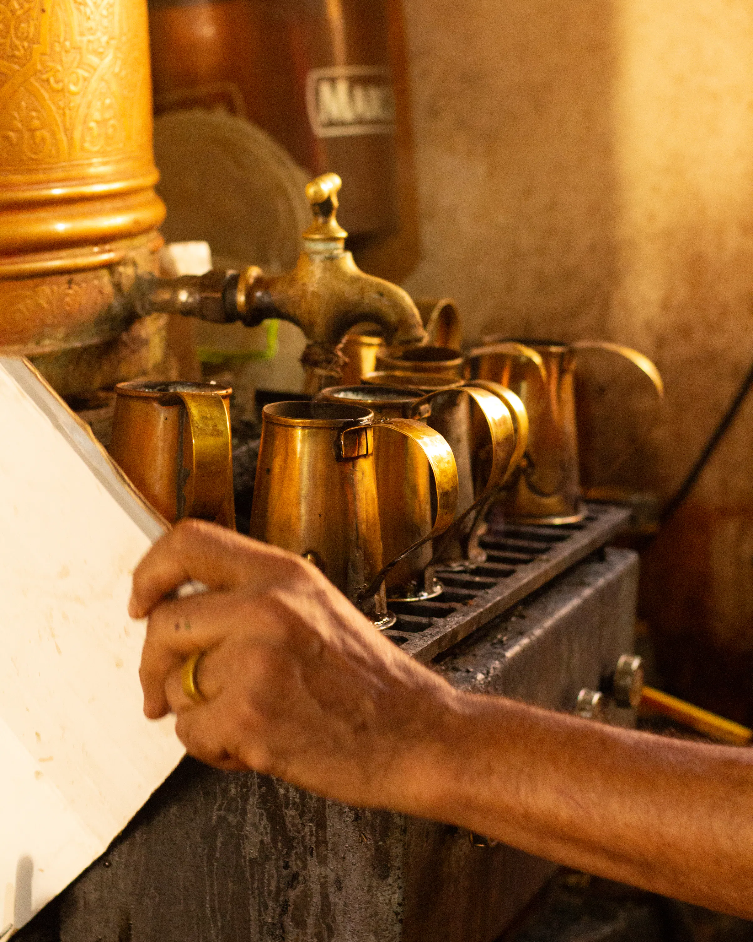 Close-up of tea being poured from a brass tap into small metal cups.