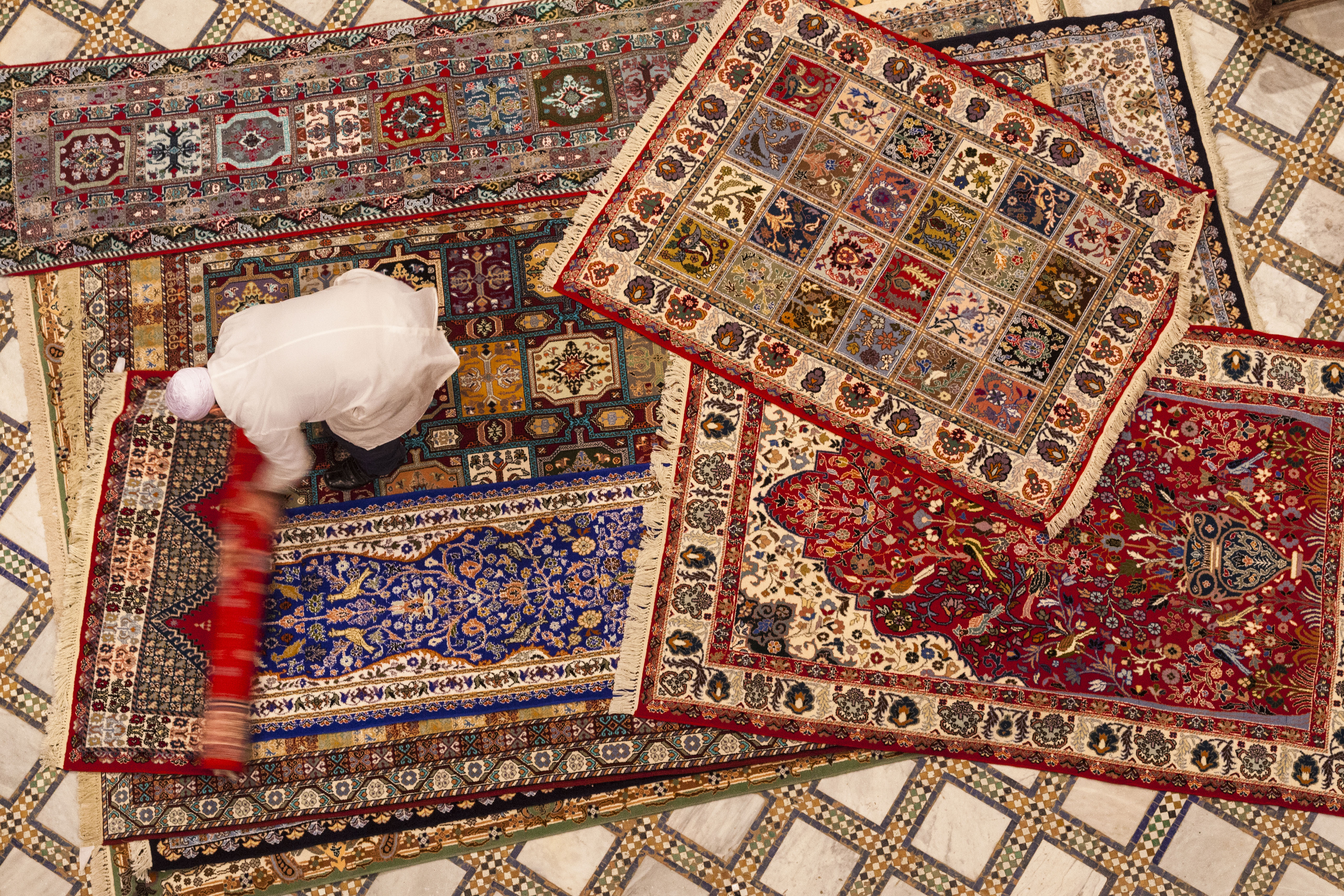 Overhead view of vibrant patterned Moroccan rugs layered across a tiled floor.