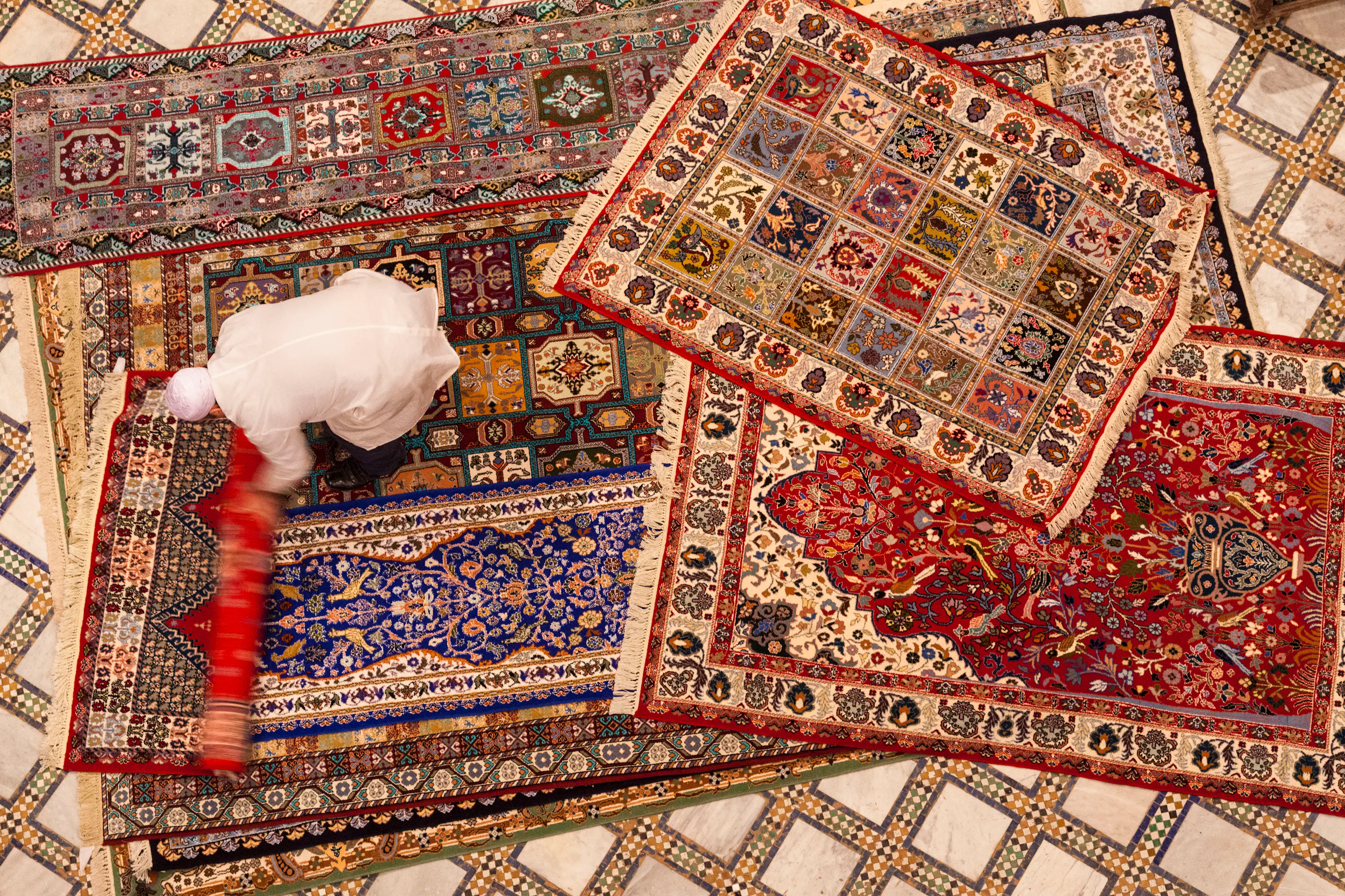 Overhead view of vibrant patterned Moroccan rugs layered across a tiled floor.