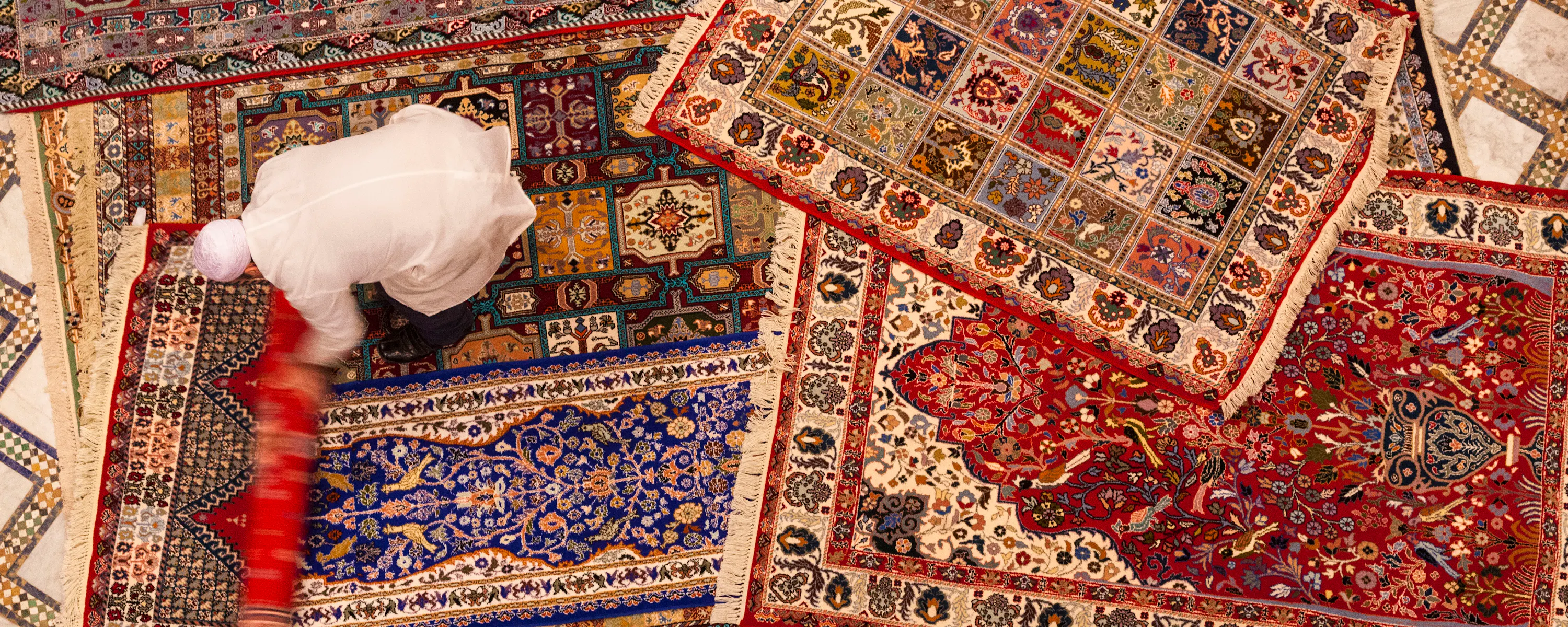 Overhead view of vibrant patterned Moroccan rugs layered across a tiled floor.