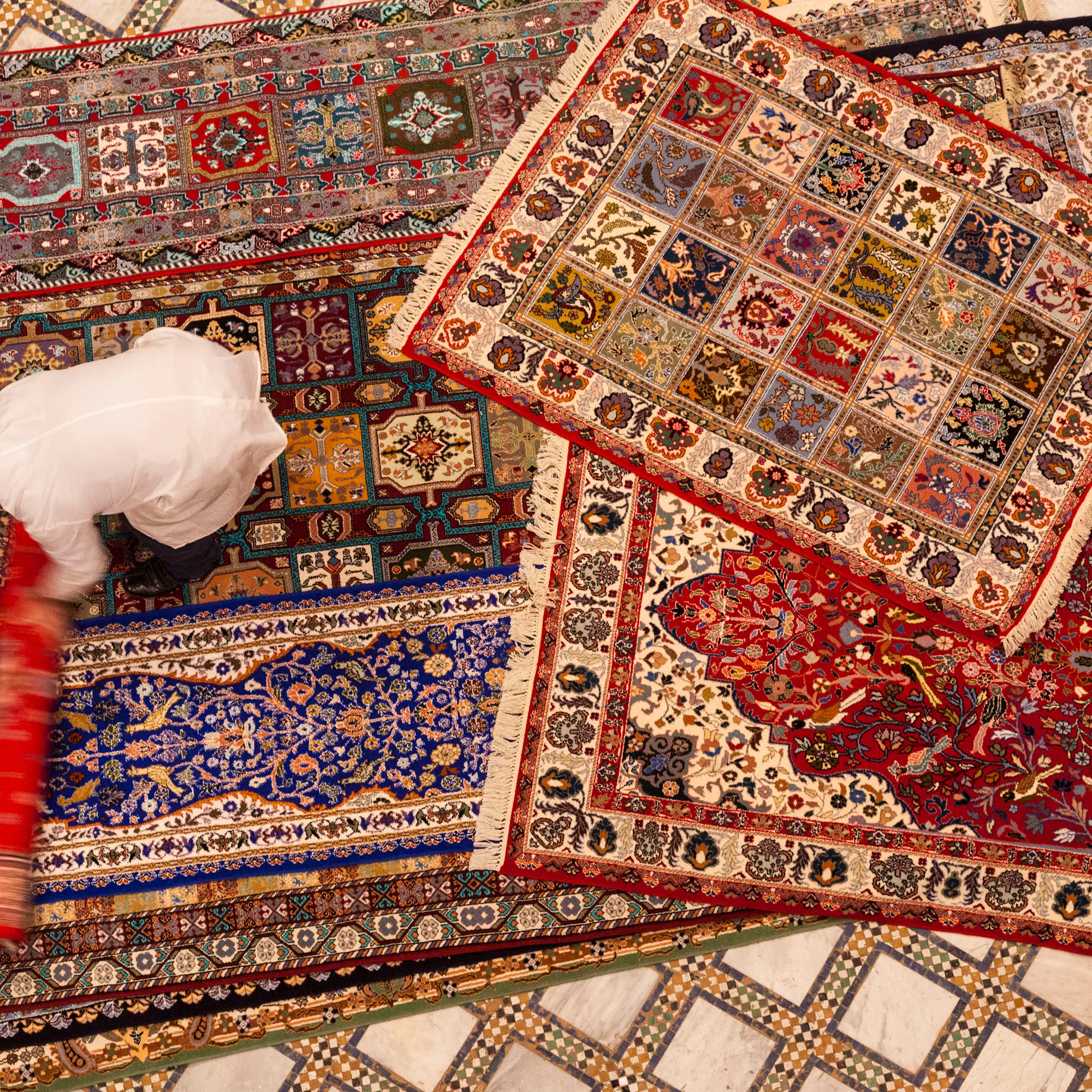 Overhead view of vibrant patterned Moroccan rugs layered across a tiled floor.