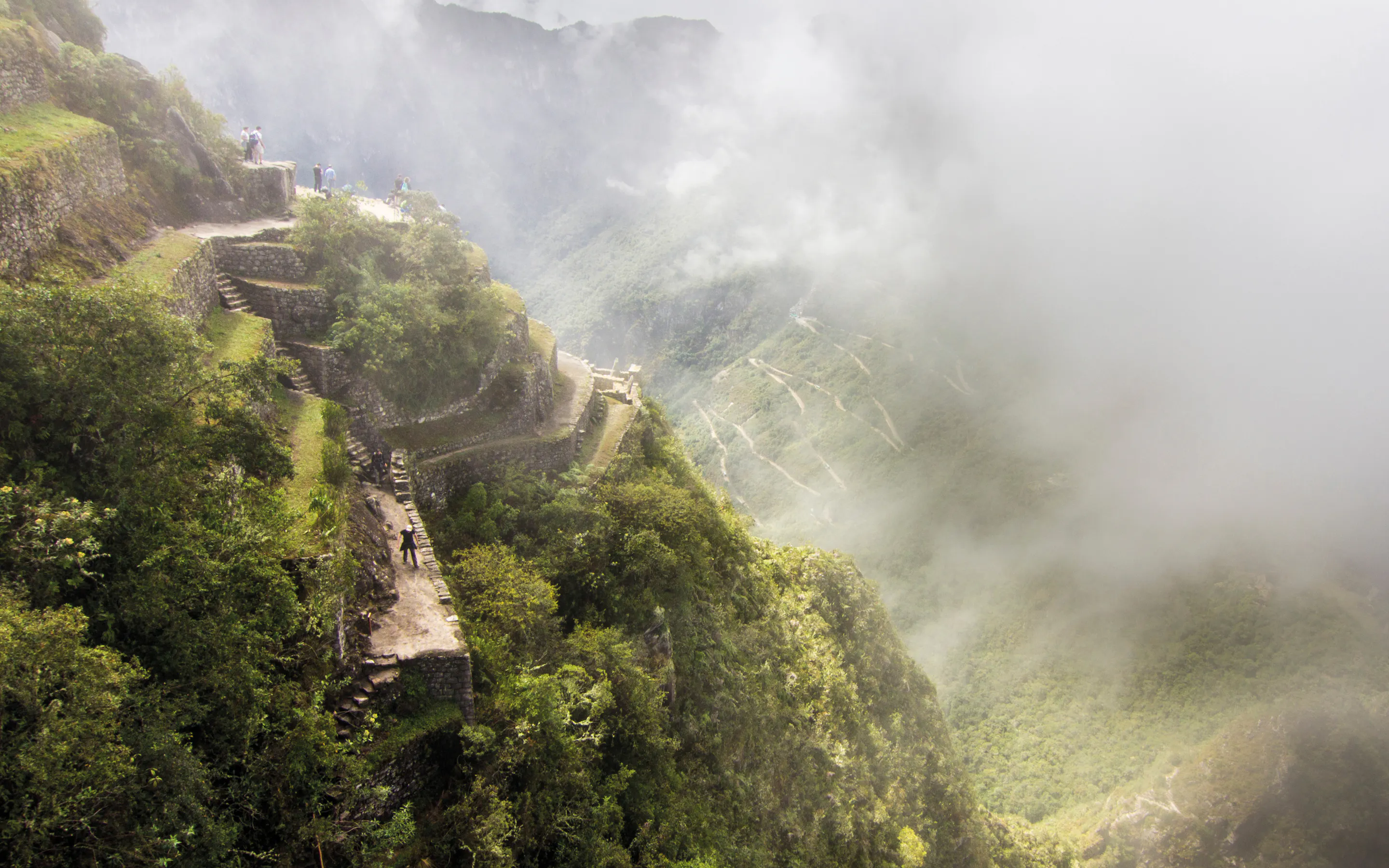 Ancient stone terraces and pathways on a steep mountainside, partially obscured by mist and clouds.