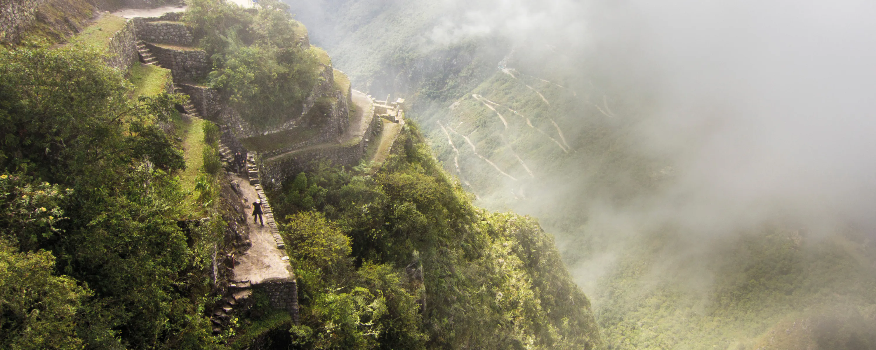 Ancient stone terraces and pathways on a steep mountainside, partially obscured by mist and clouds.