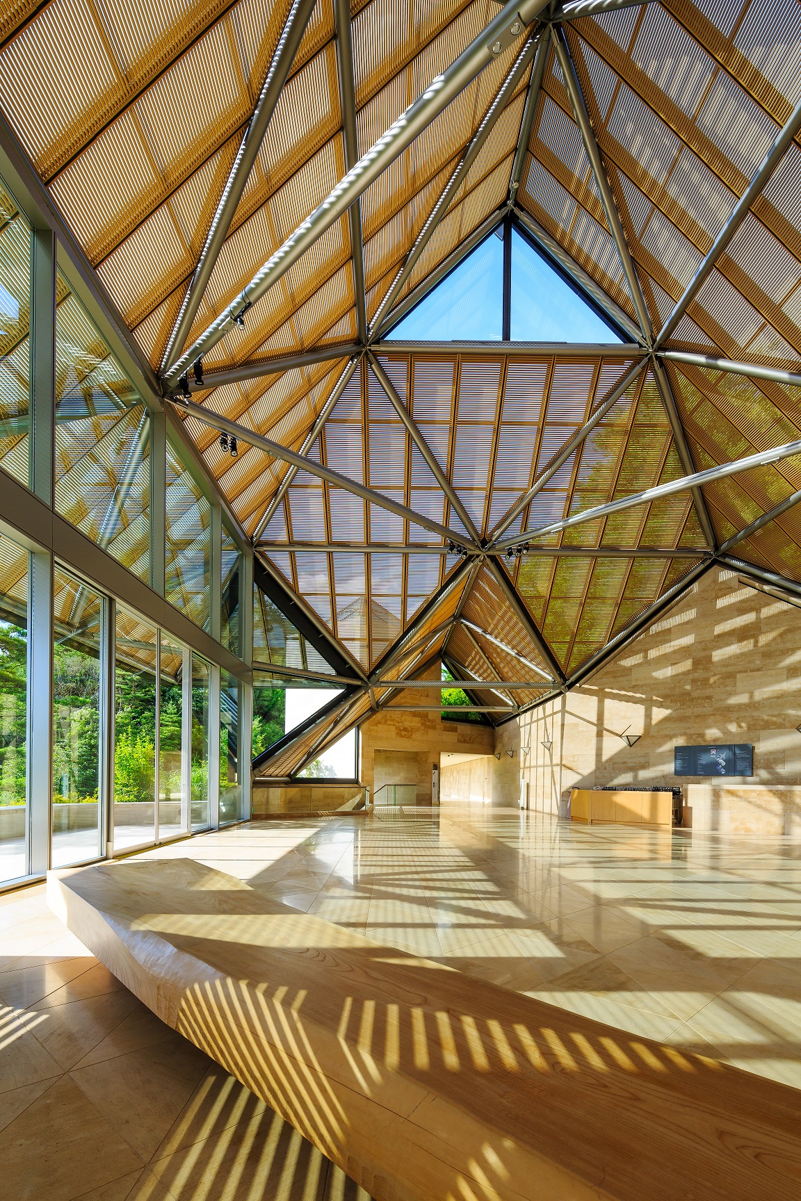Sunlight fills MIHO Museum's geometric entrance hall, where glass walls and a faceted timber roof frame the interior.