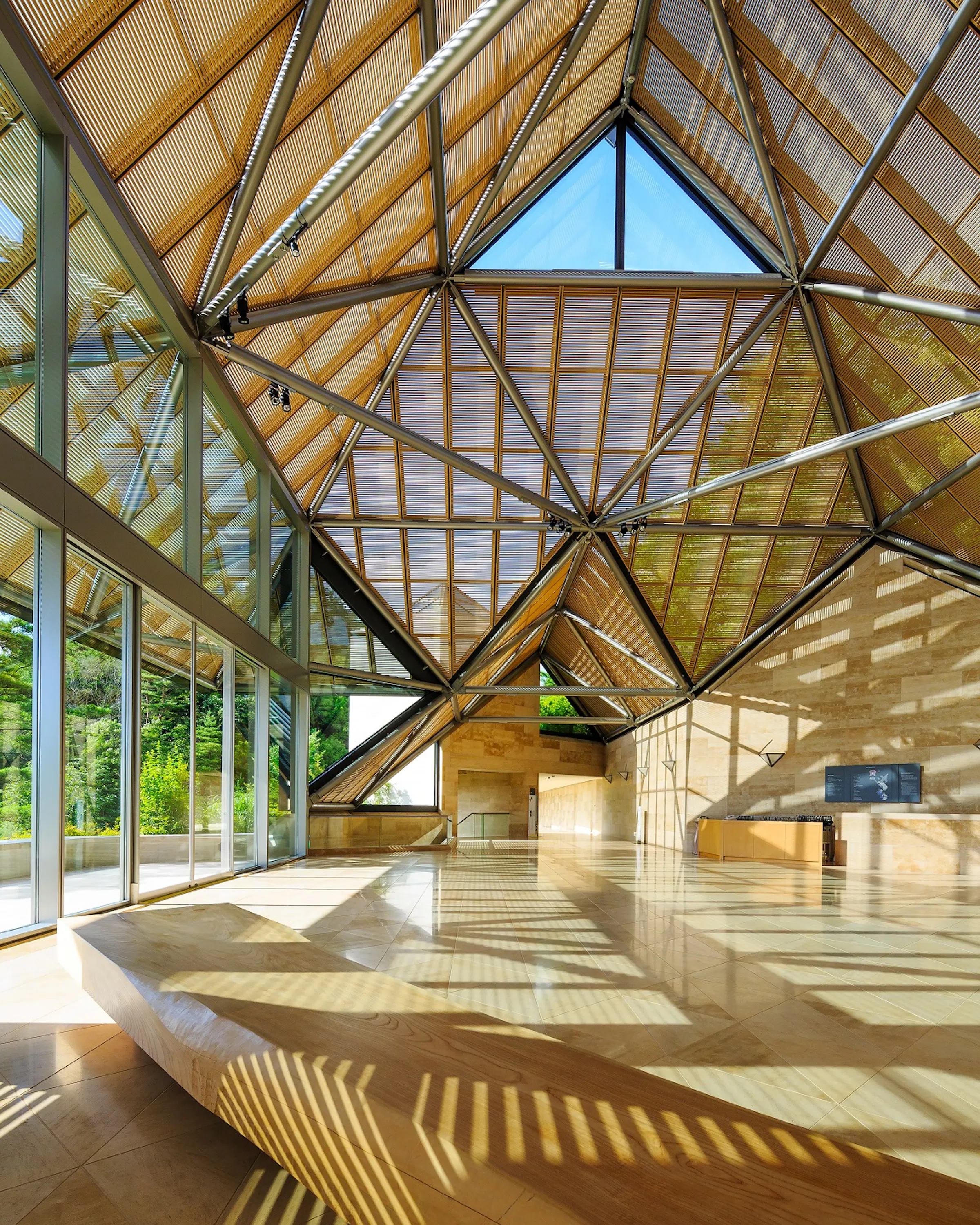 Sunlight fills MIHO Museum's geometric entrance hall, where glass walls and a faceted timber roof frame the interior.
