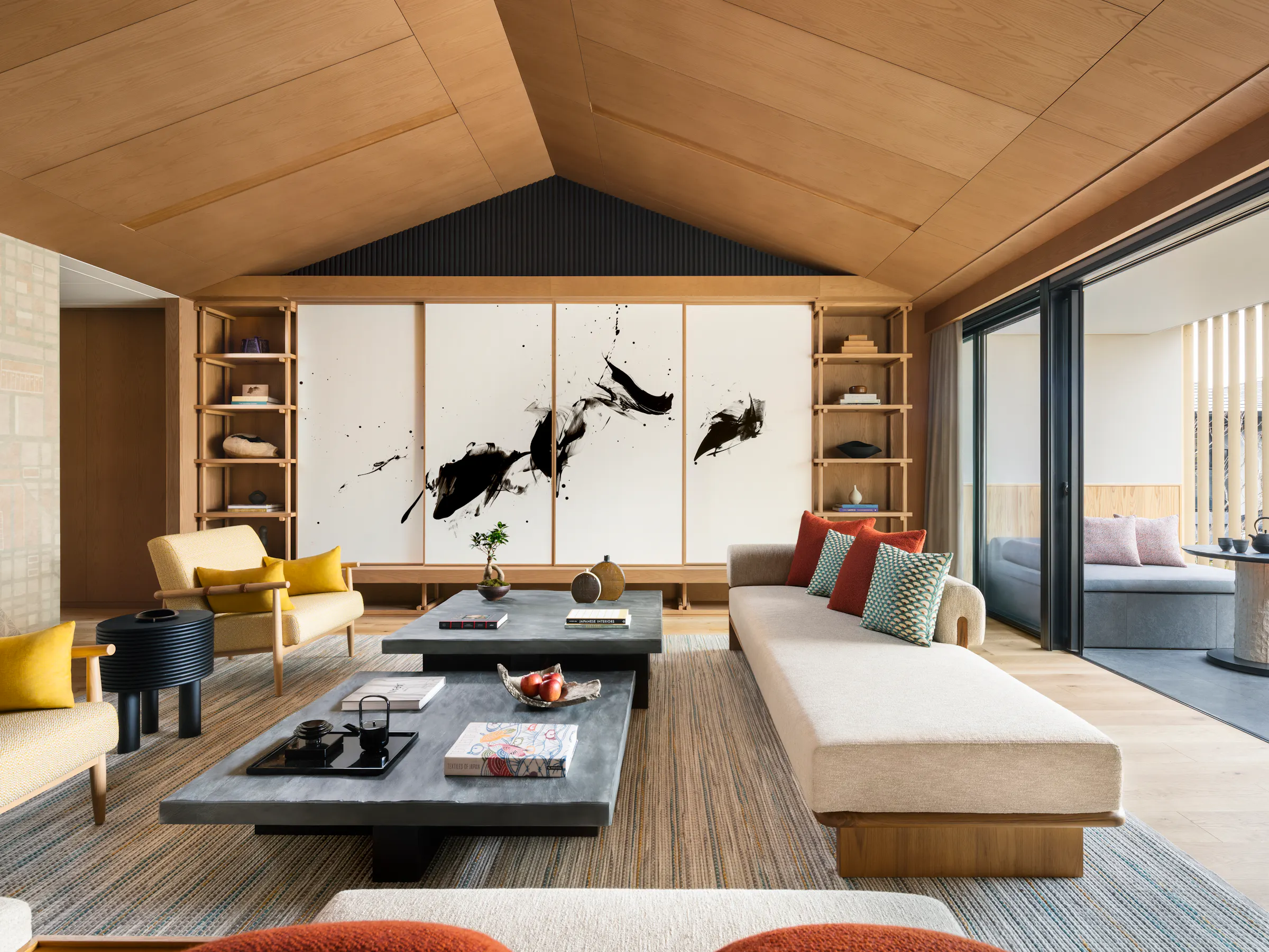 A serene living room at Six Senses Kyoto features low tables, pale wood, bold artwork, and a covered terrace beyond.