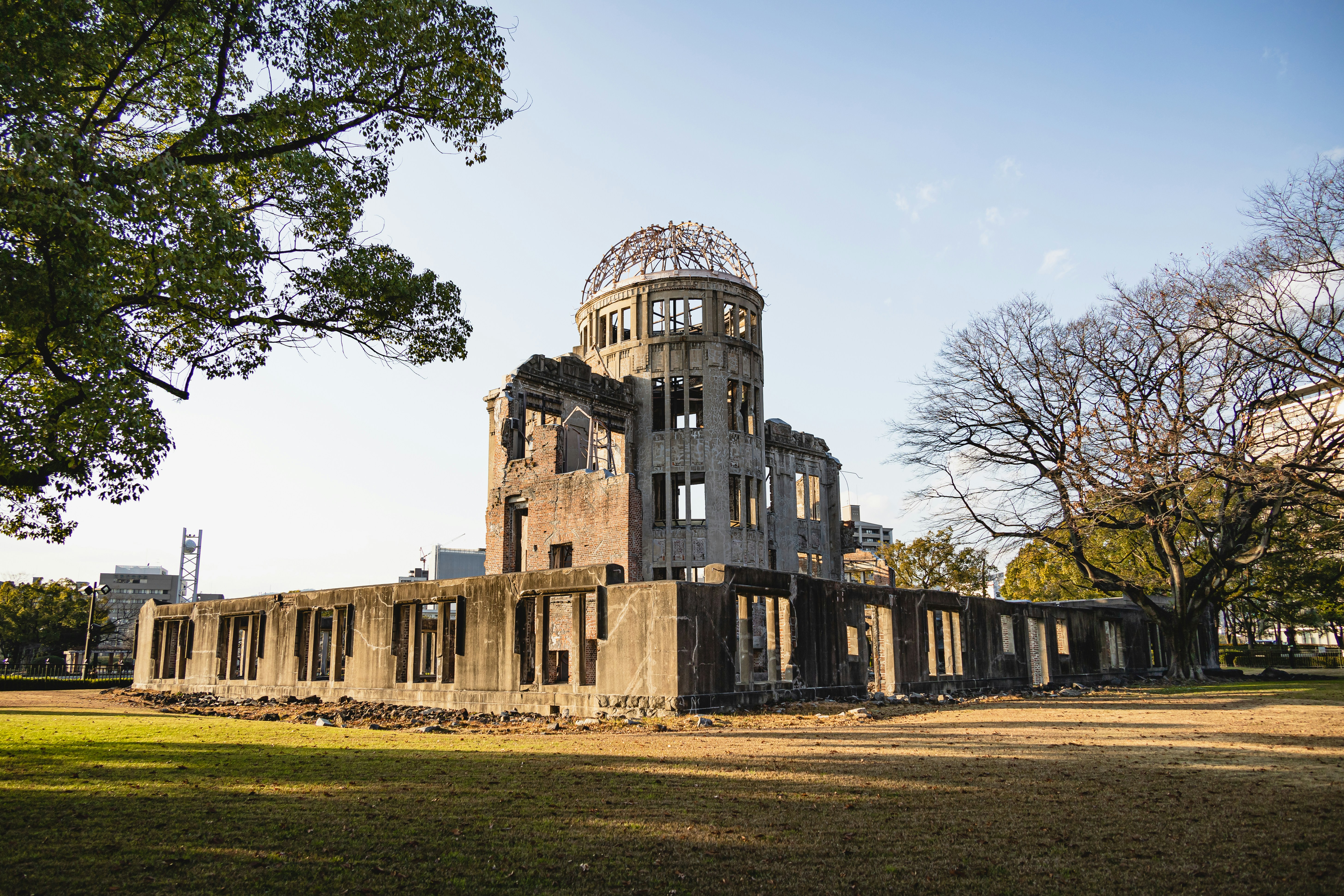 The Atomic Bomb Dome stands in warm light above the lawn, framed by broad trees and the surviving concrete walls.