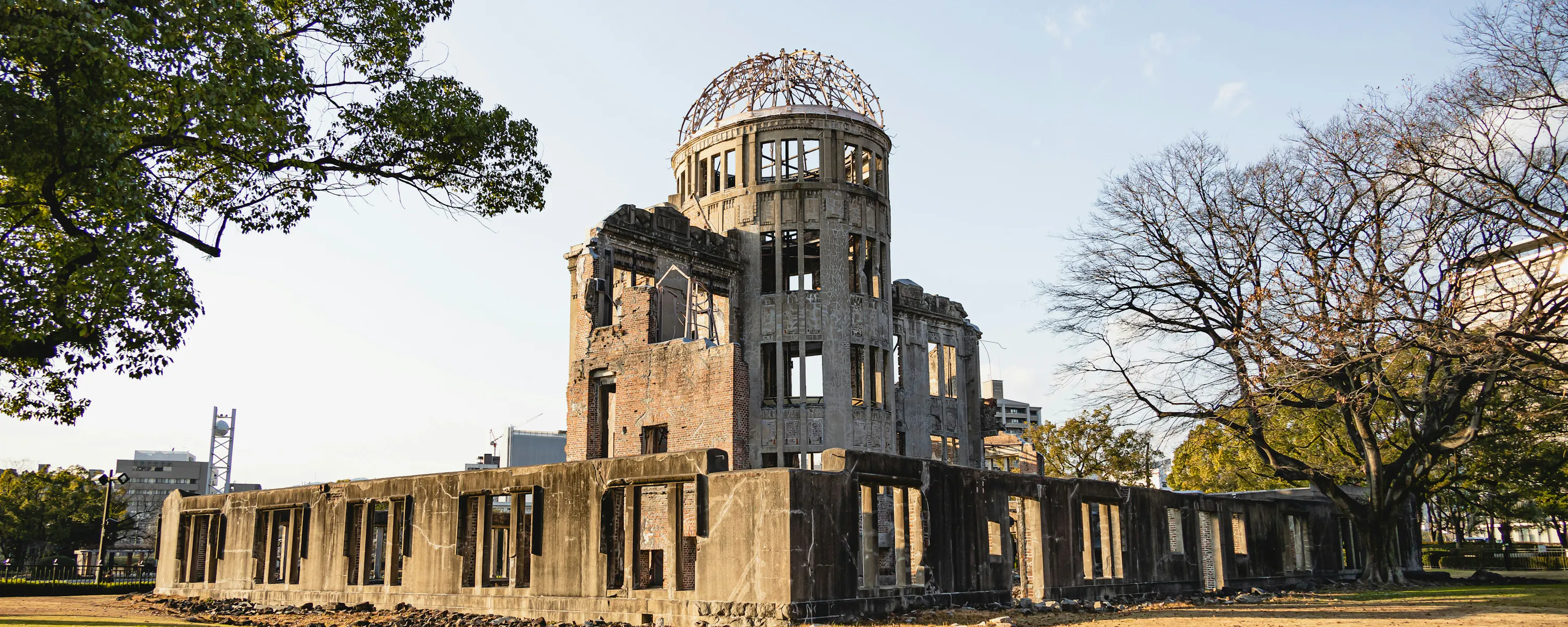 The Atomic Bomb Dome stands in warm light above the lawn, framed by broad trees and the surviving concrete walls.