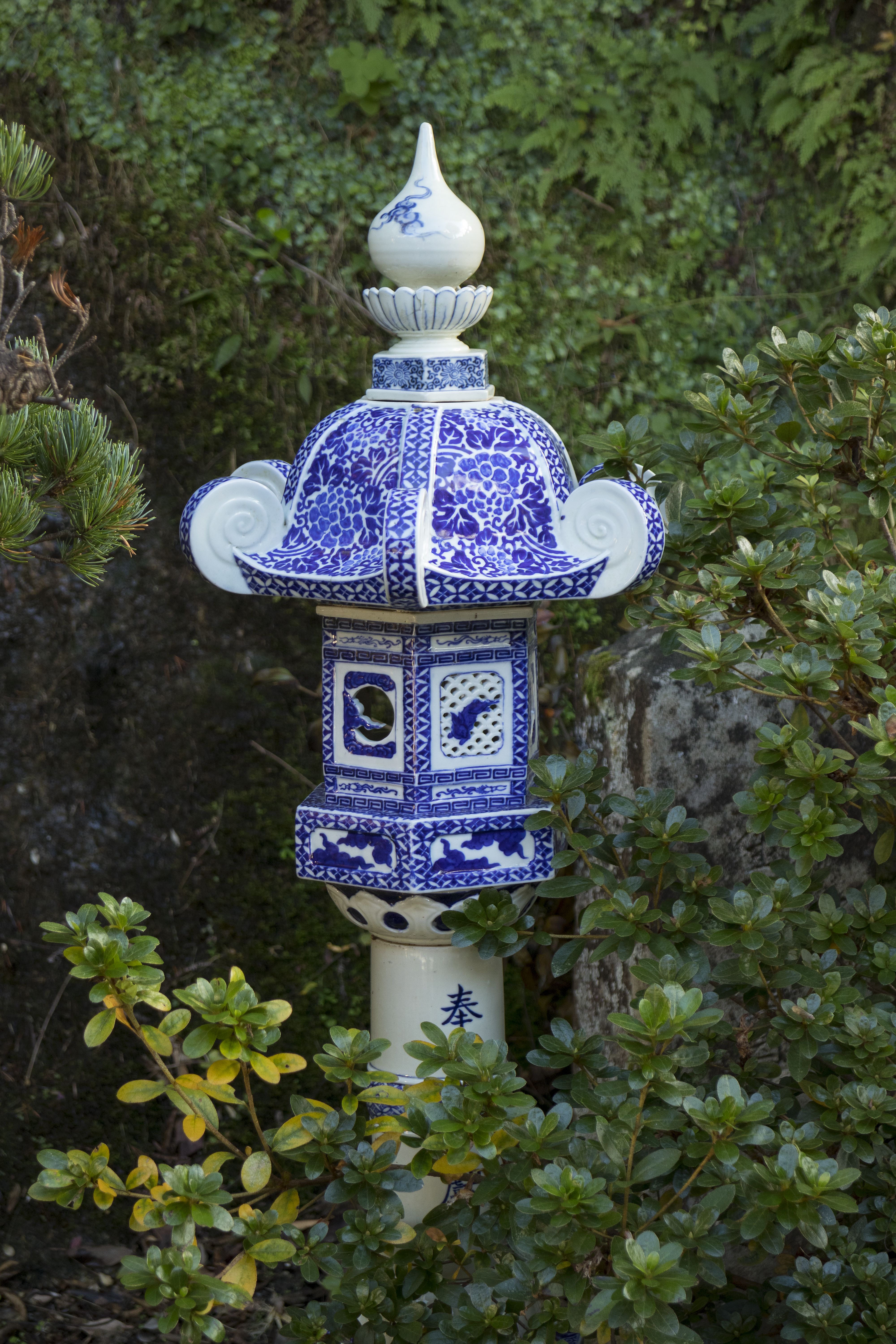 A blue-and-white lantern stands among green shrubs at Tozan Shrine in Arita, showing delicate porcelain patterns.