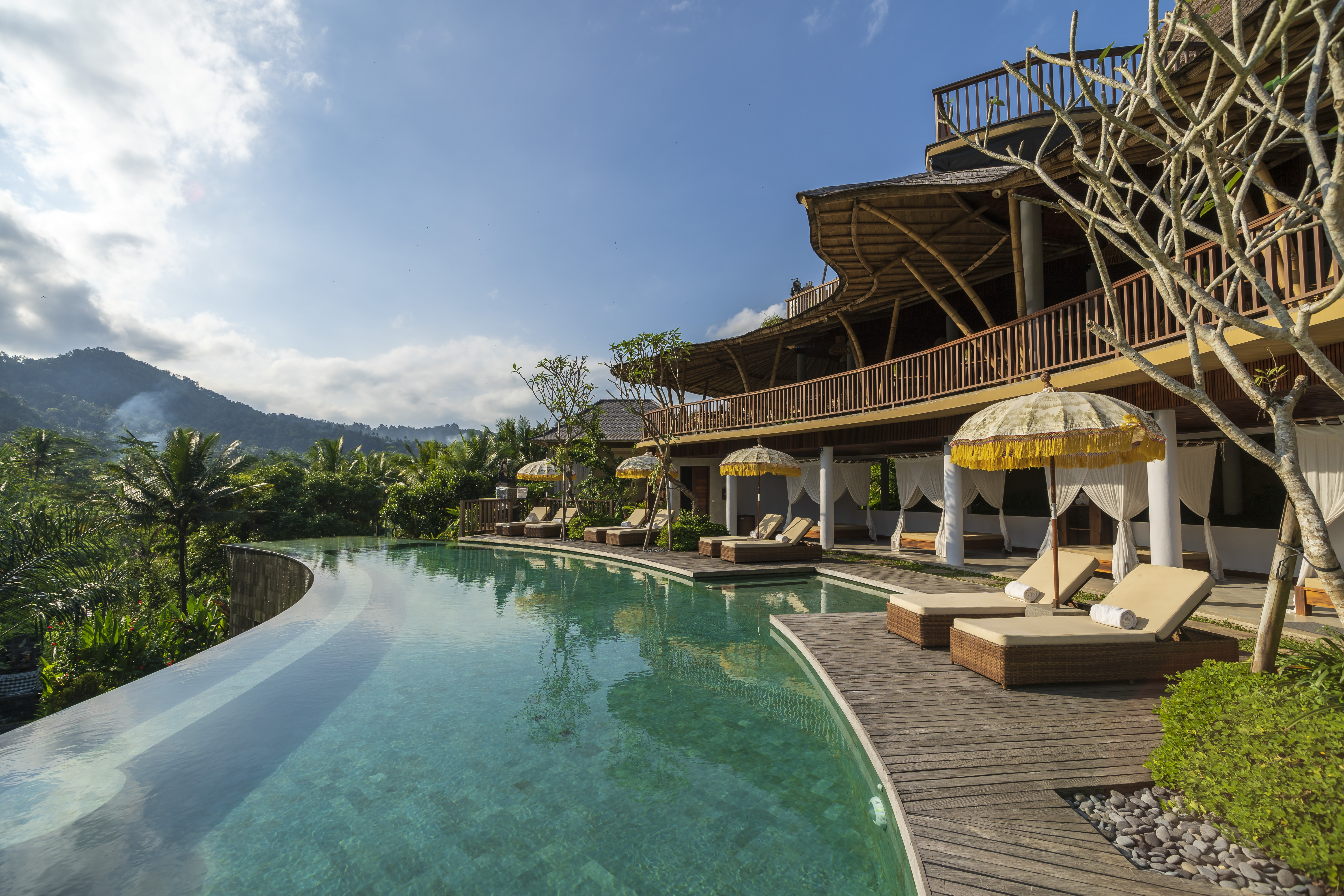An infinity pool curves past loungers and pavilions at Wapa Di Ume Sidemen, with hills rising beyond the palms.