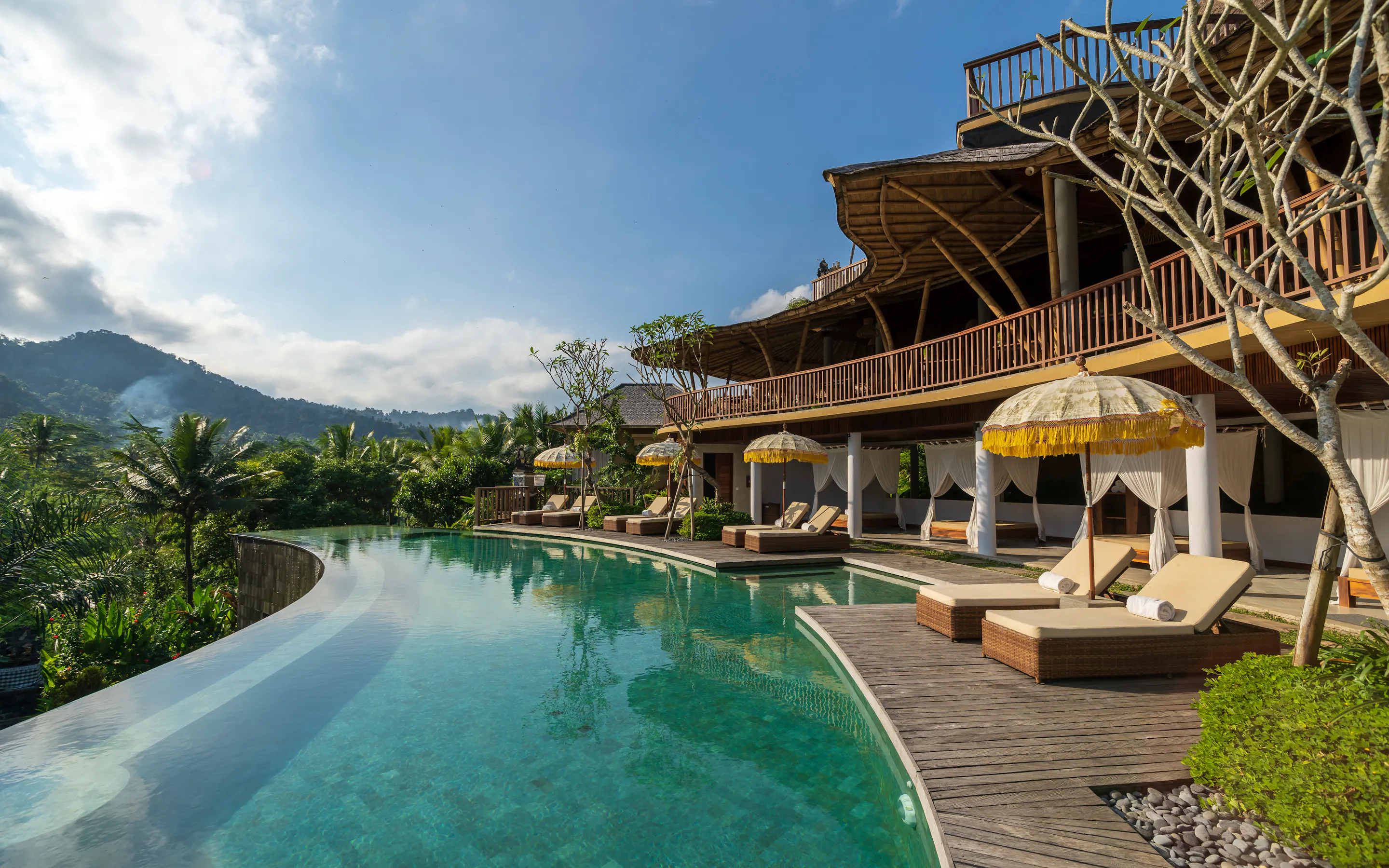 An infinity pool curves past loungers and pavilions at Wapa Di Ume Sidemen, with hills rising beyond the palms.